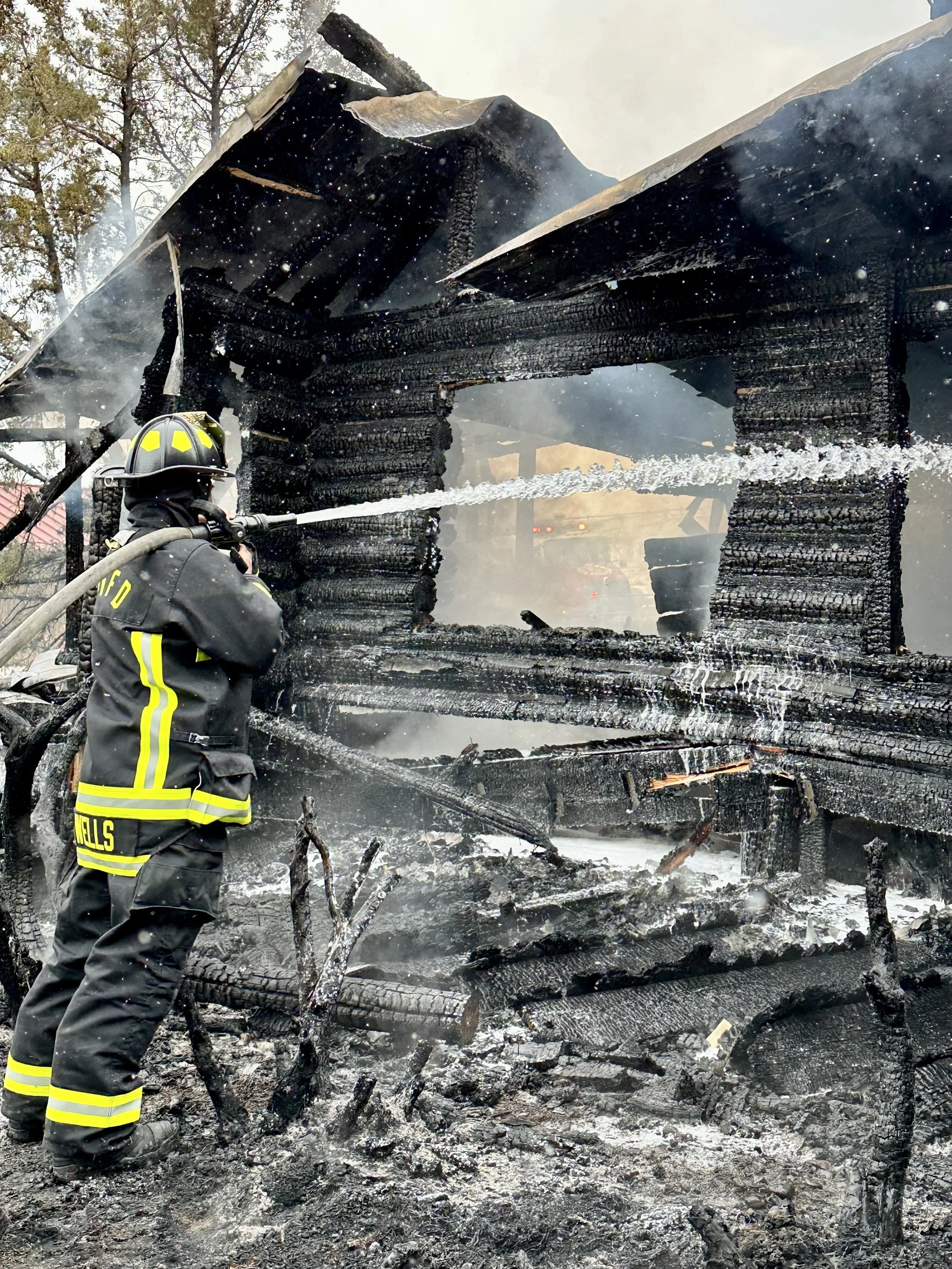 Firefighter spraying water on the remains of a burnt, charred house during a fire scene.