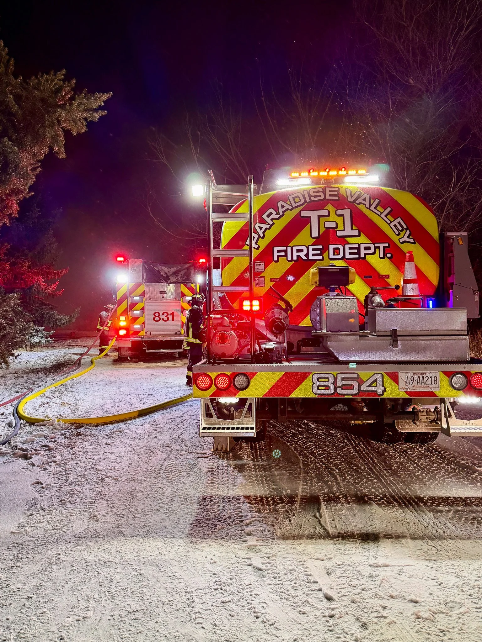Fire truck from Paradise Valley Fire Department at night on snowy ground, with firefighters handling hoses.