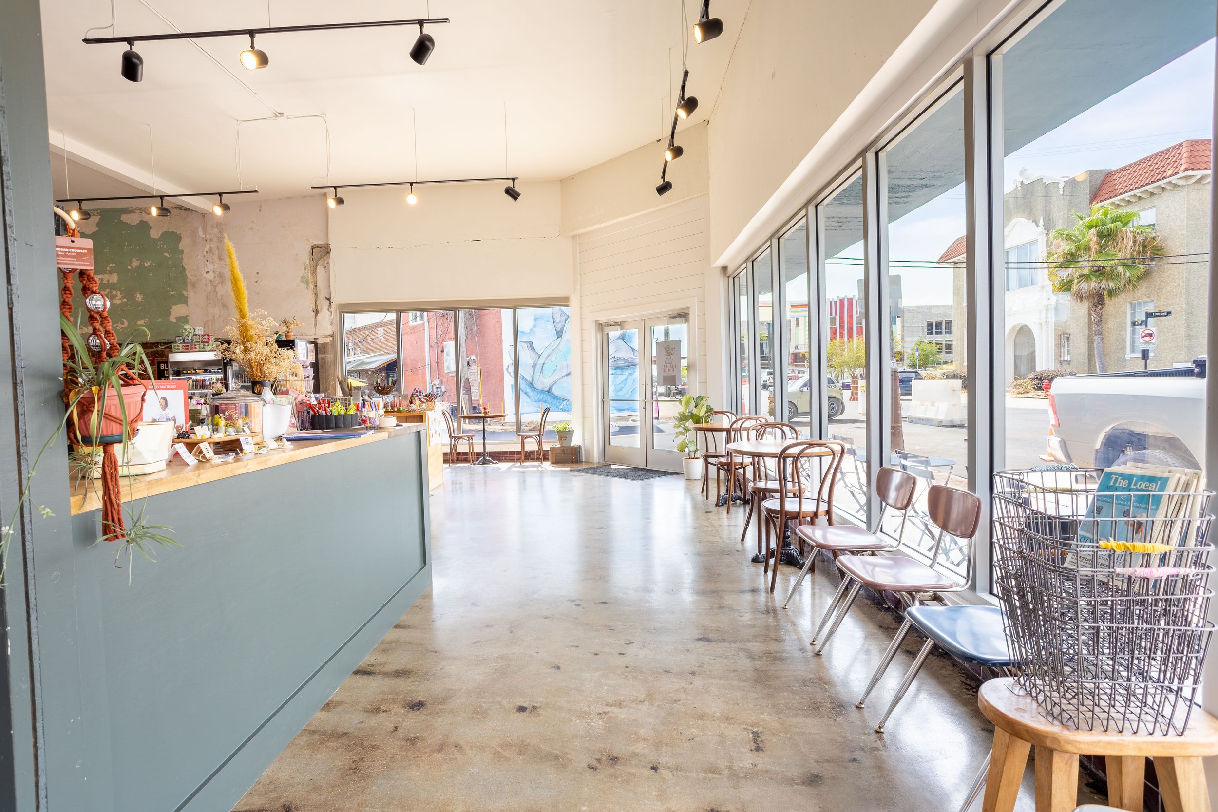 Inside of a modern coffee shop or cafe with large glass windows, seating area with chairs, and a counter with plants and decorative items.