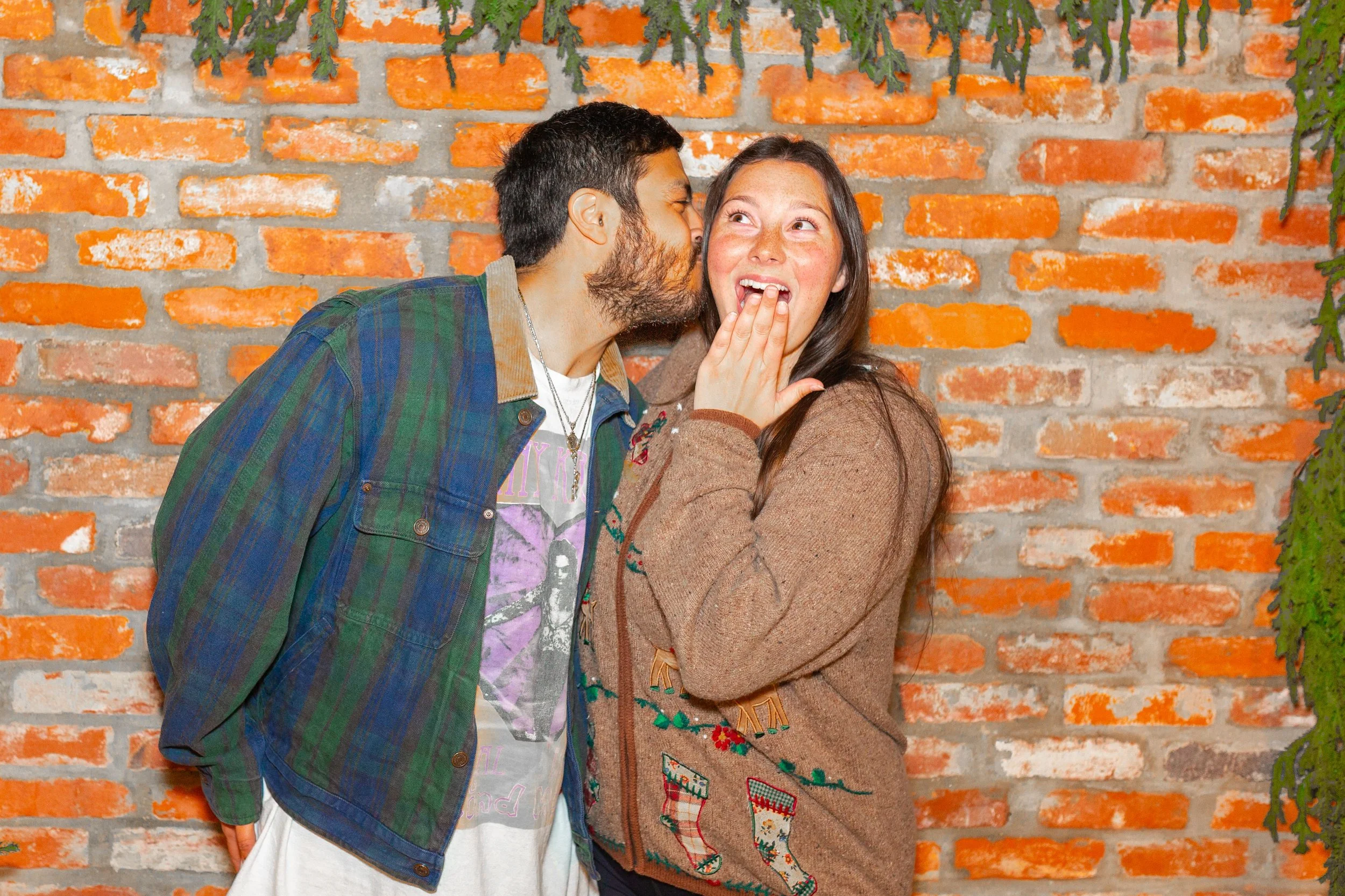 A man and woman sharing a secret in front of a brick wall.