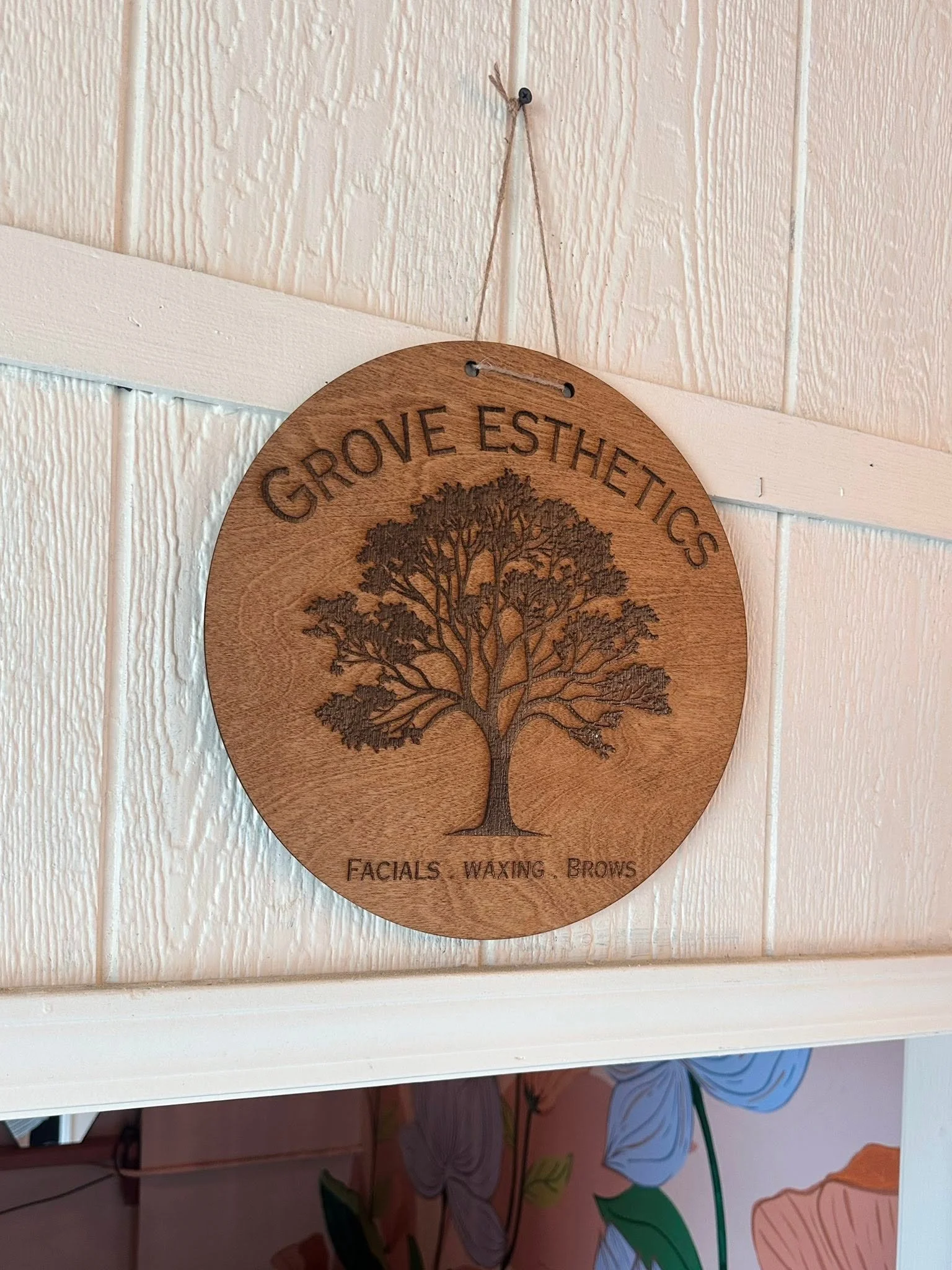 Wooden Grove Esthetics studio sign displaying the business logo and facial, waxing, and brow services. Interior branding for a Panama City, Florida esthetics studio specializing in customized facials, skincare treatments, brows, and waxing.