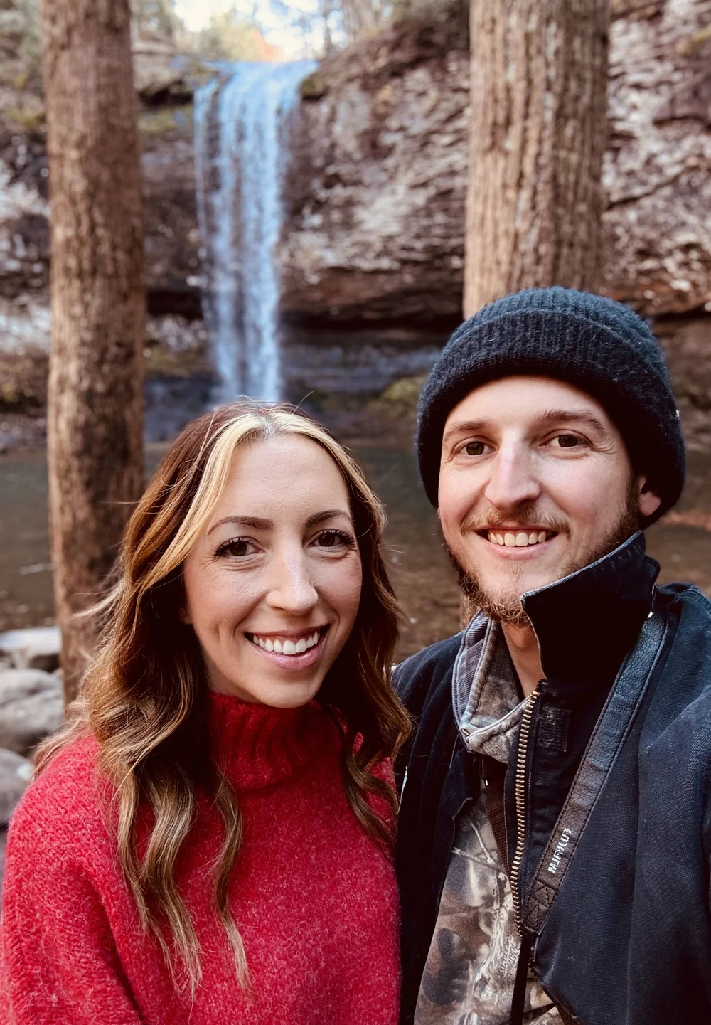 Two people smiling in front of a waterfall