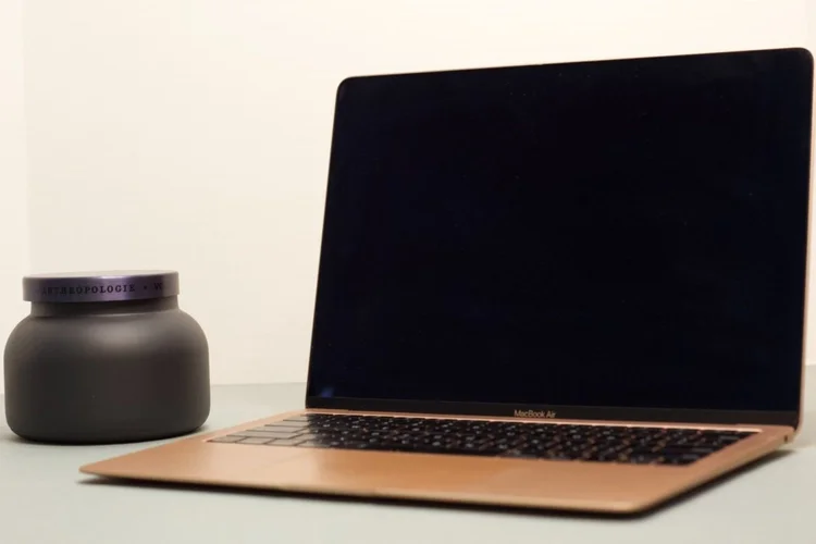 Laptop on a desk beside a dark candle jar