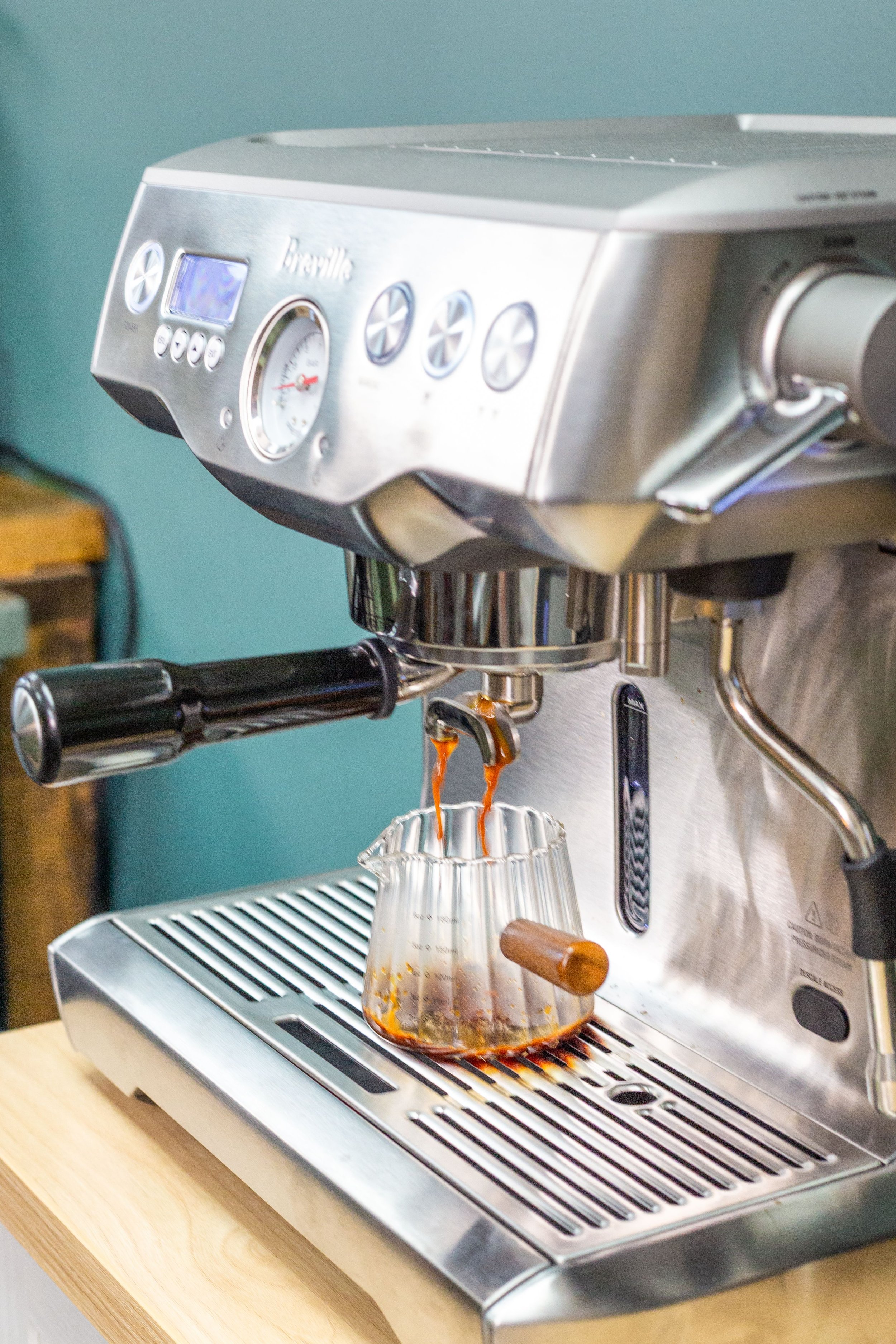 A stainless steel espresso machine brewing coffee into a glass cup, with steam and coffee dripping from the spout.