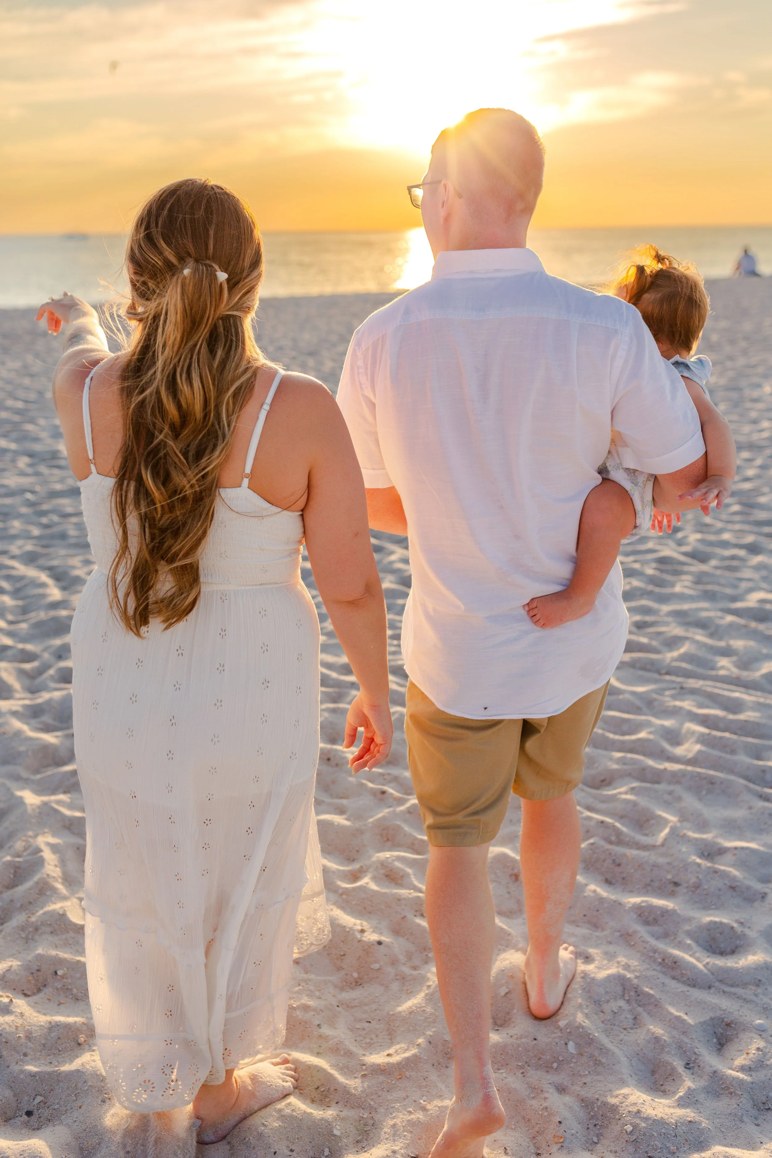 A family walking on the beach during sunset, with the mother and father carrying their young child.