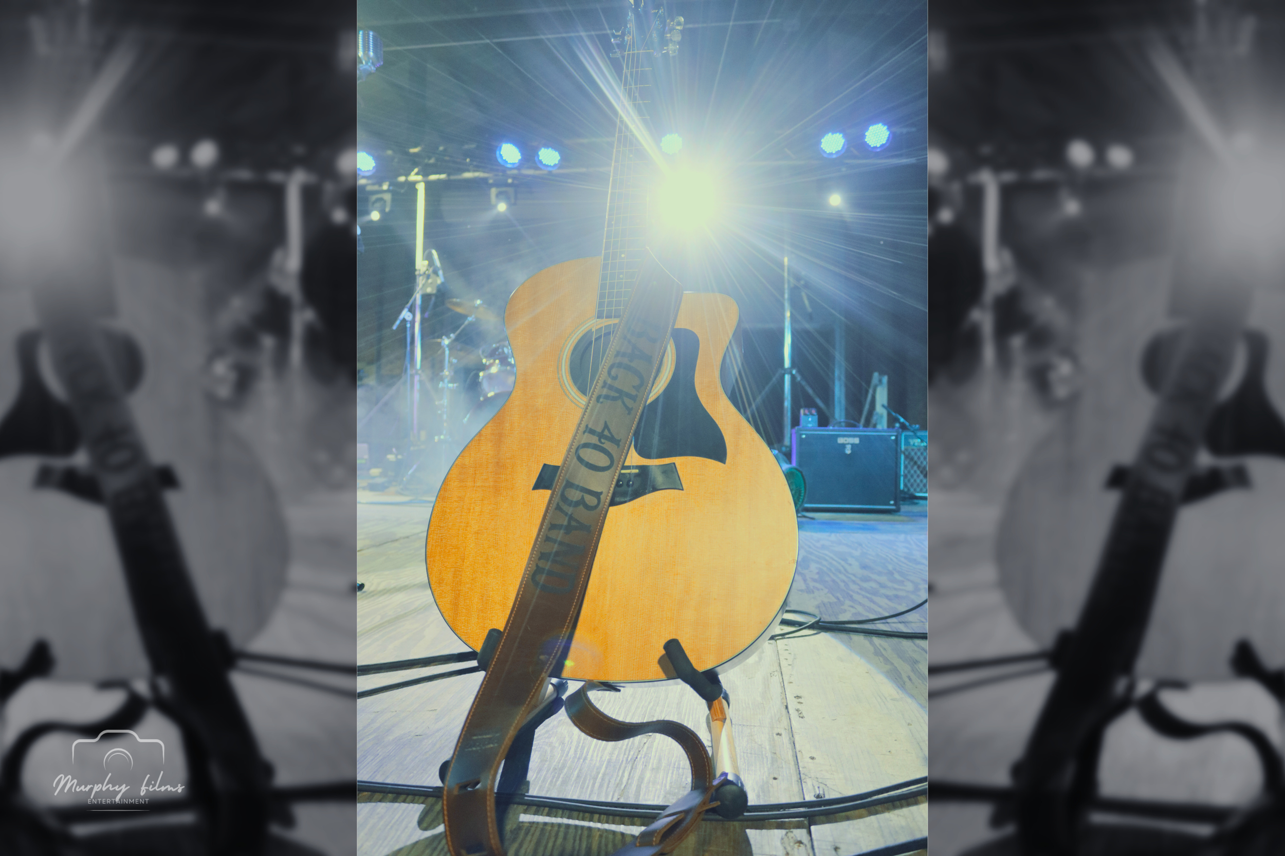 An acoustic guitar on a stand on a stage with bright lights and musical equipment in the background.