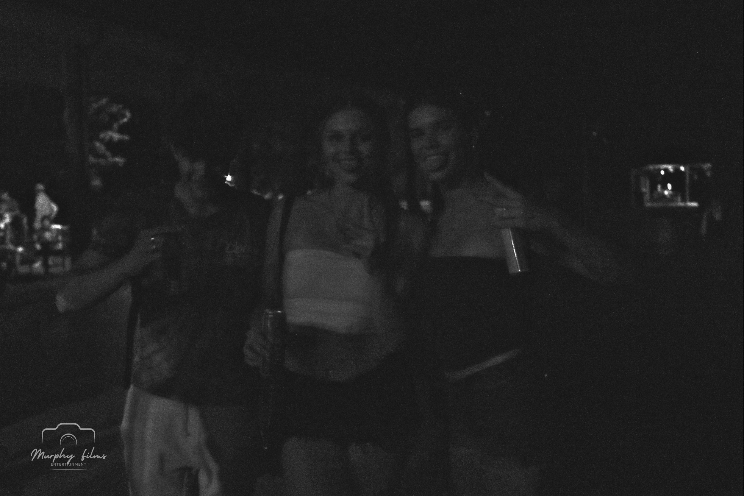 Three people holding drinks at night outside, smiling and posing for the camera.