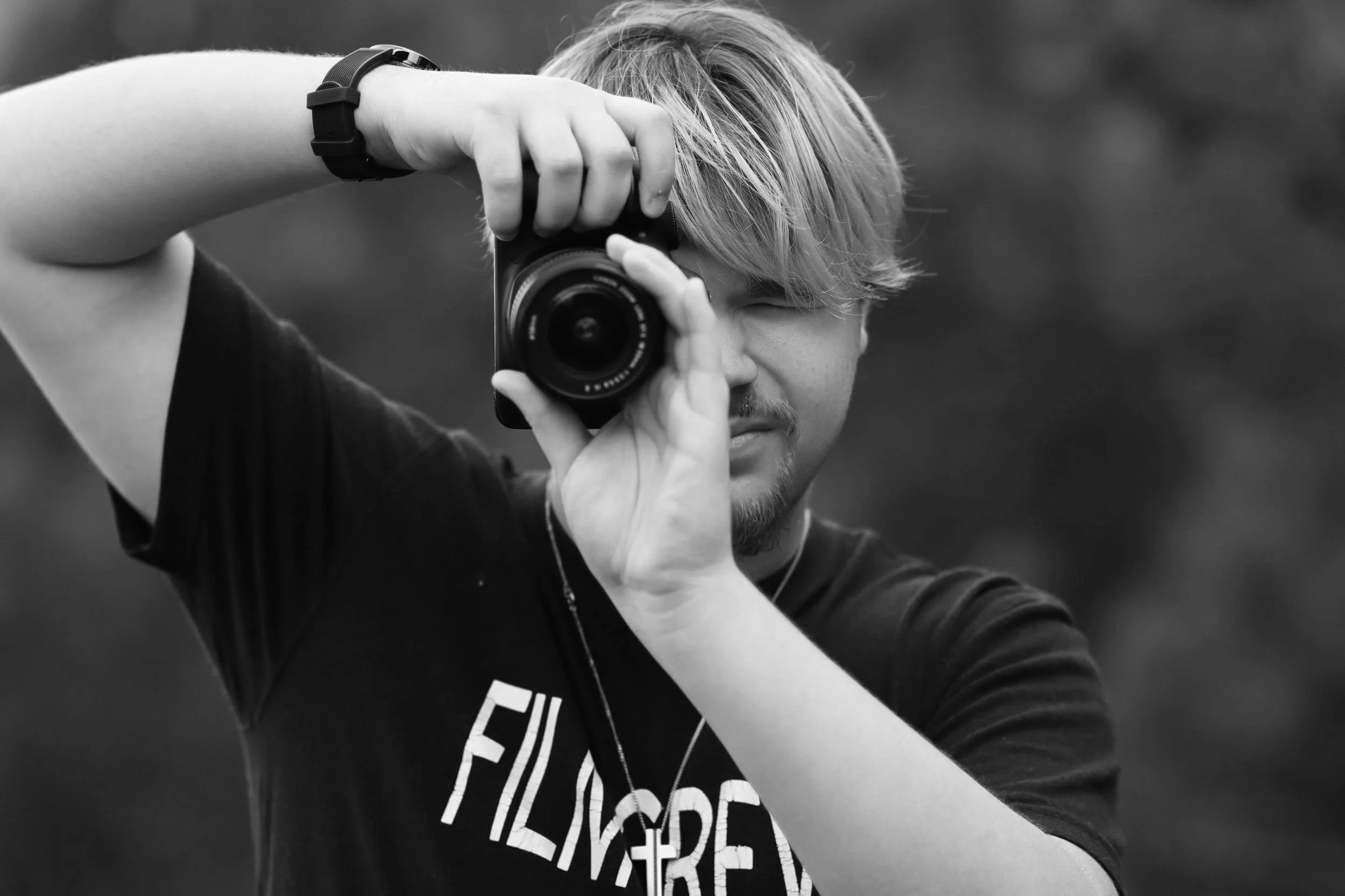 Person taking a photo with a camera, wearing a "FILM CREW" t-shirt.
