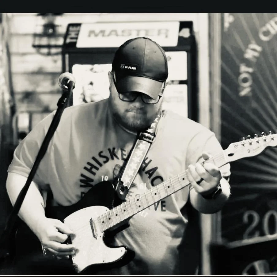 A man wearing a cap and glasses playing an electric guitar in a bar or music venue.