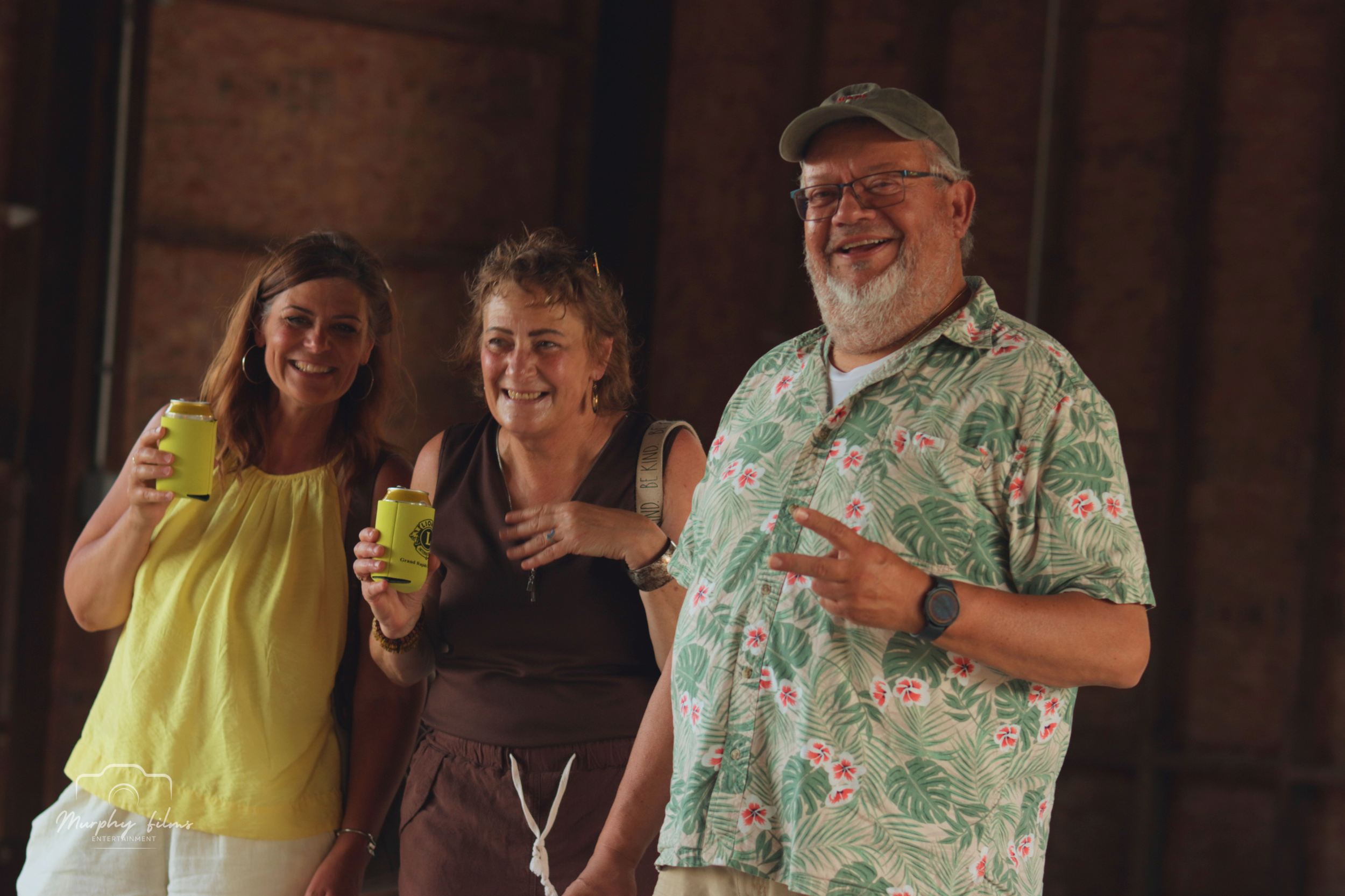 Three smiling people standing together, holding drinks, at a casual indoor gathering.