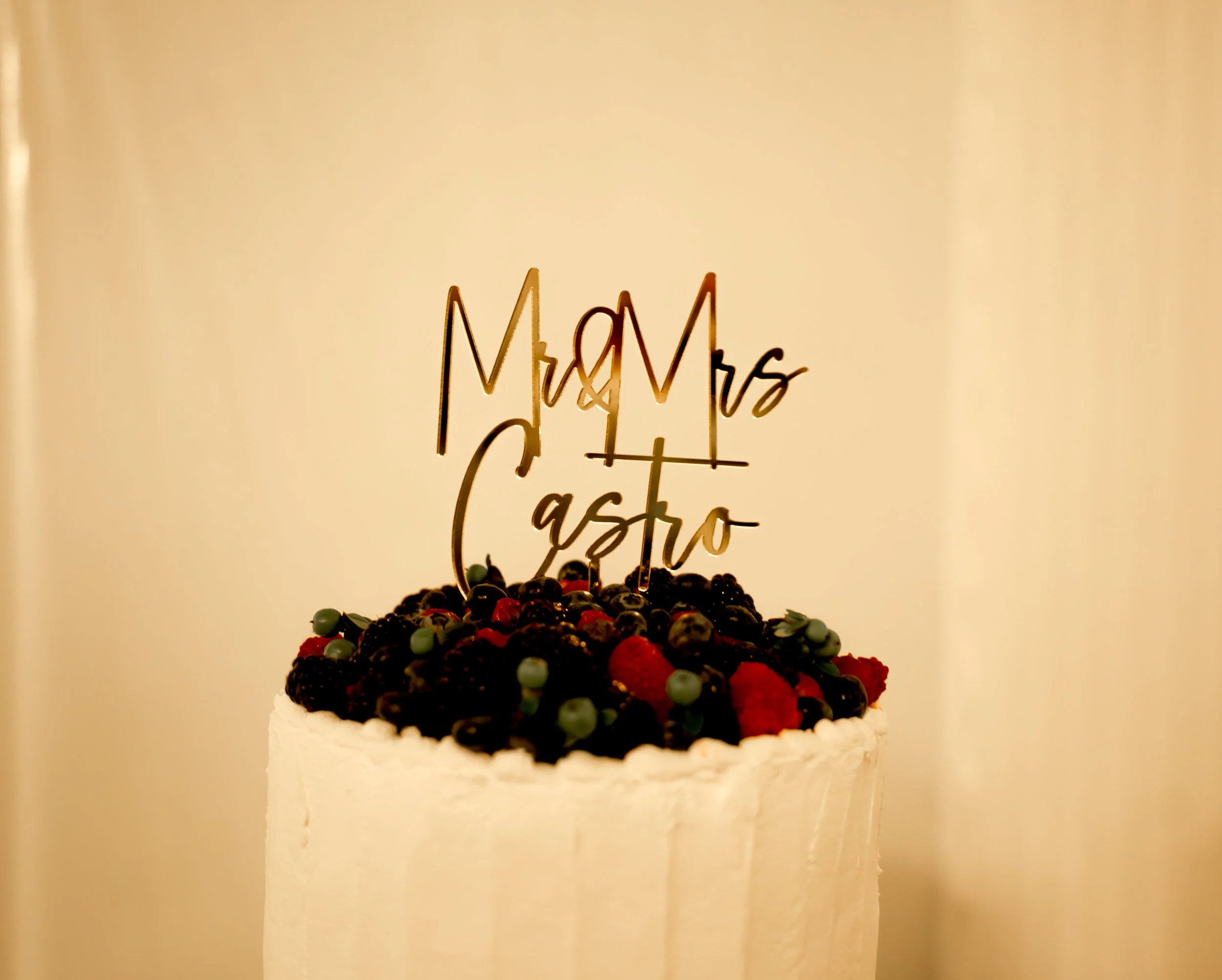 A birthday cake decorated with berries and a topper that reads 'Mr & Mrs Castro'.