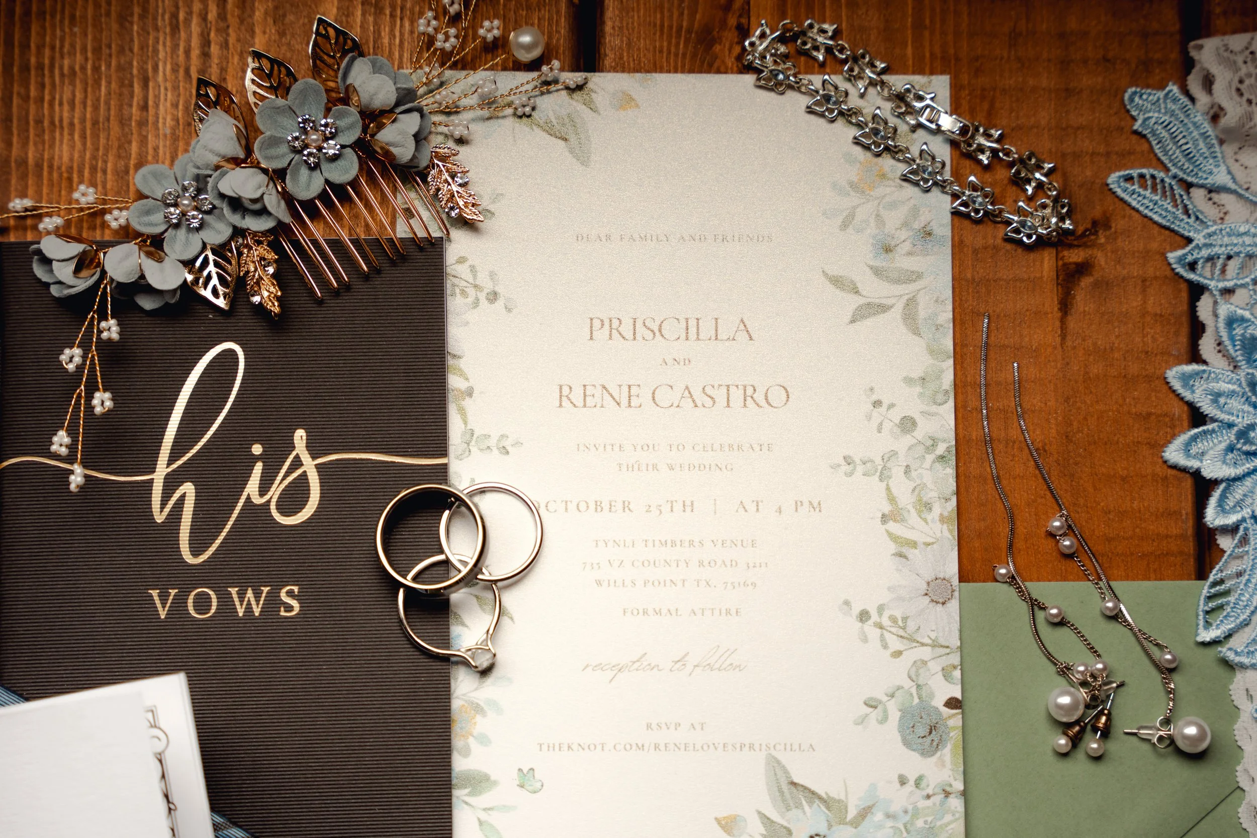 Wedding invitation surrounded by jewelry and decorative accessories on a wooden surface.