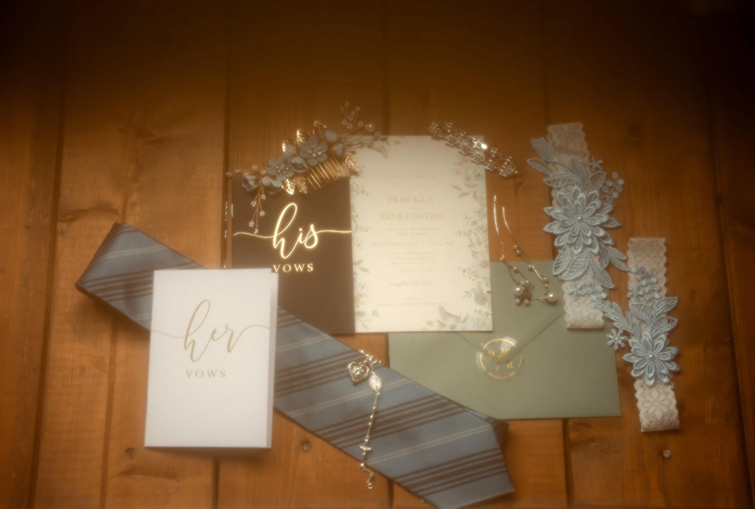Wedding invitation suite with floral accents, jewelry, lace accessories, and vows booklet arranged on a wooden surface.