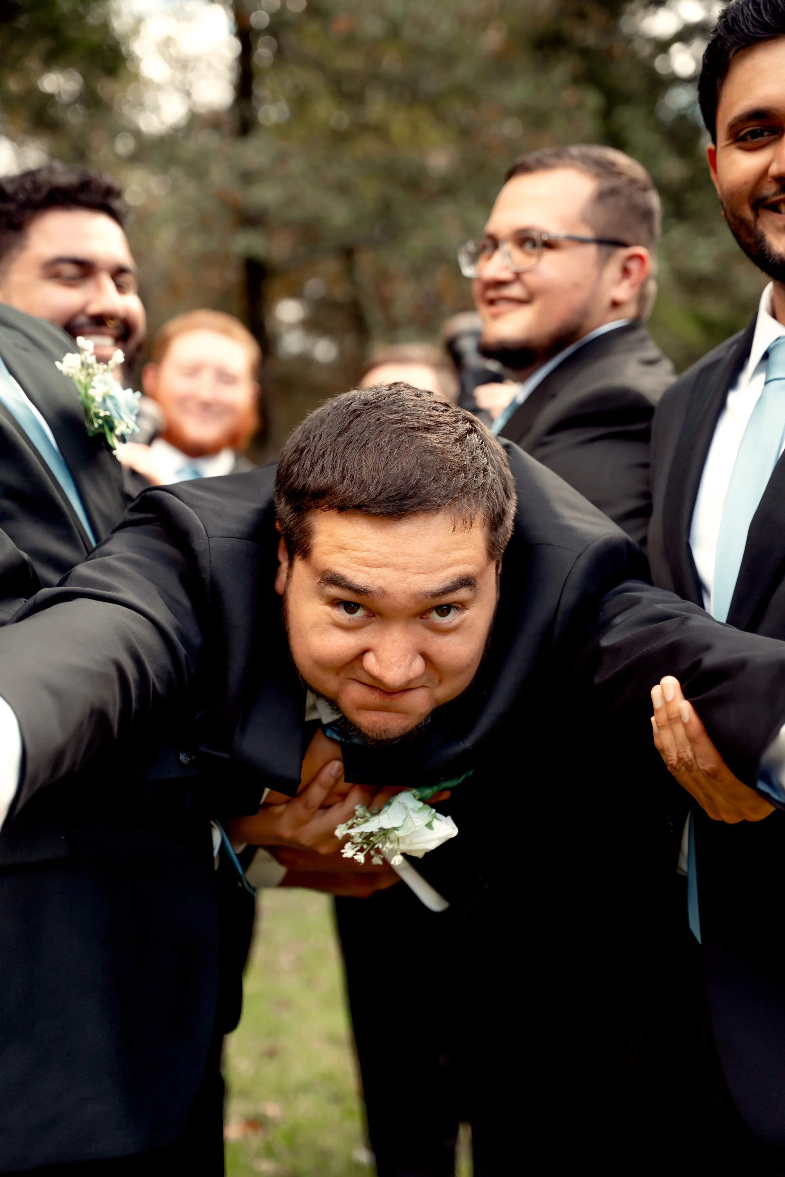 Group of men in suits and ties, celebrating outdoors, with one man playfully leaning forward in the foreground.