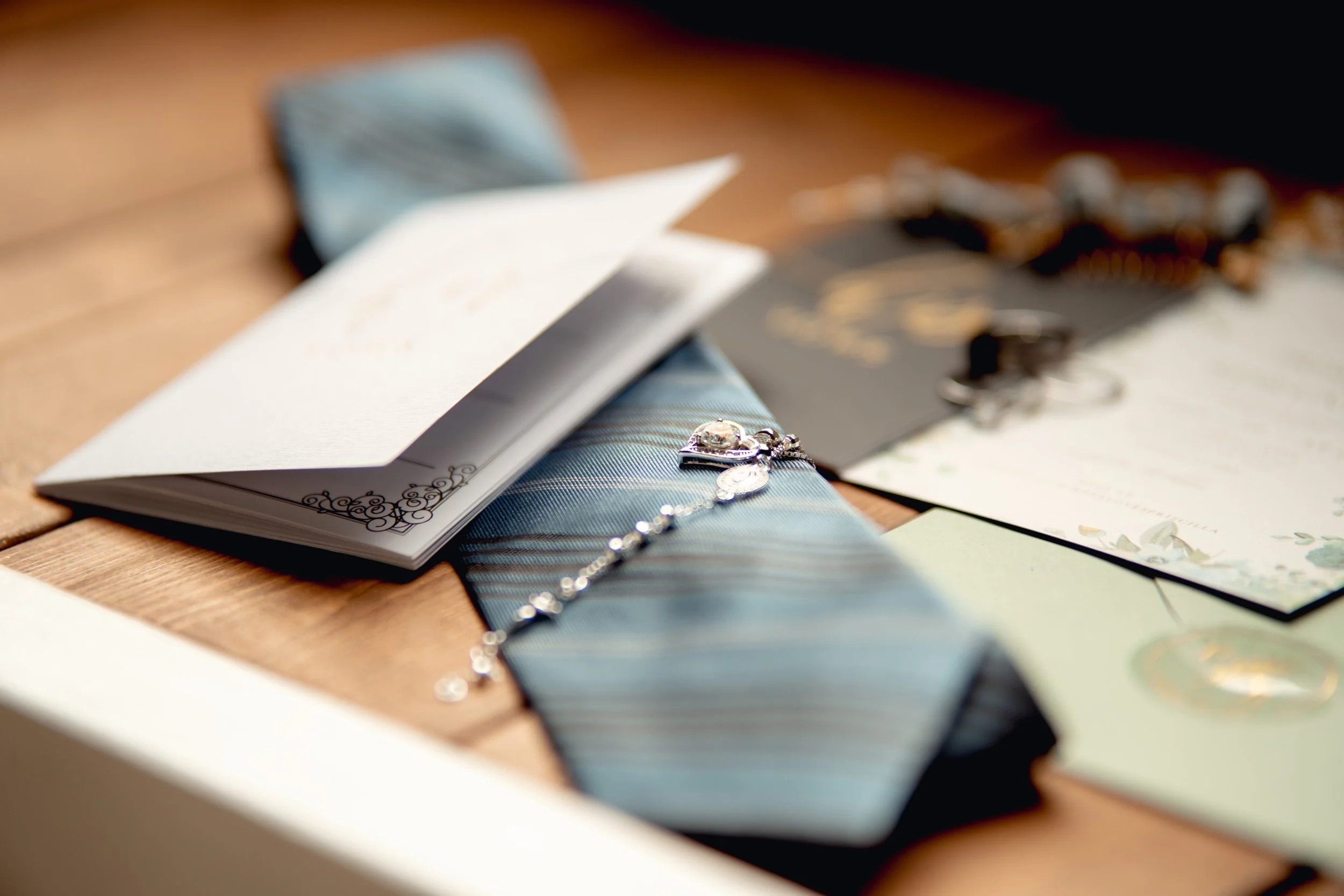 A bracelet with dangling charms and a single gem, a wedding invitation, and a small card on a wooden surface.
