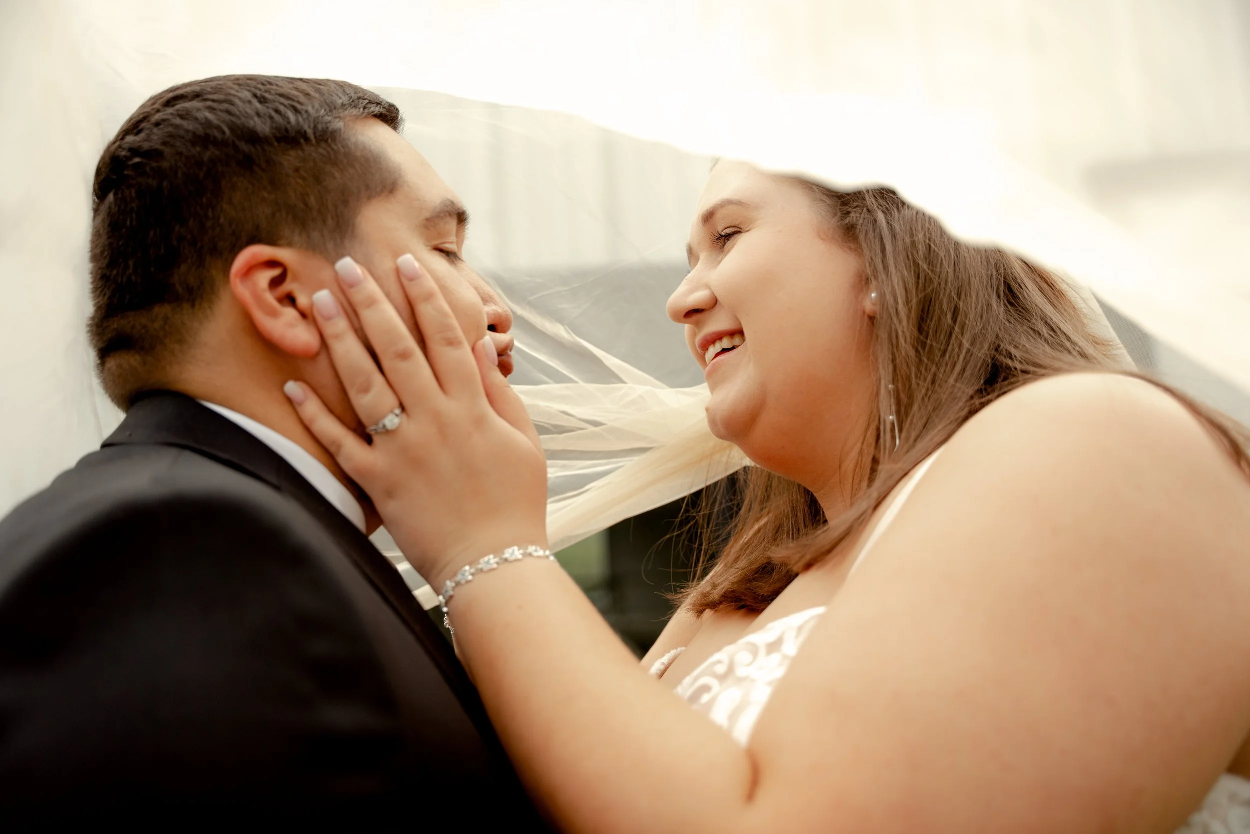 A bride and groom sharing a close moment, with the bride holding the groom's face and smiling at him.