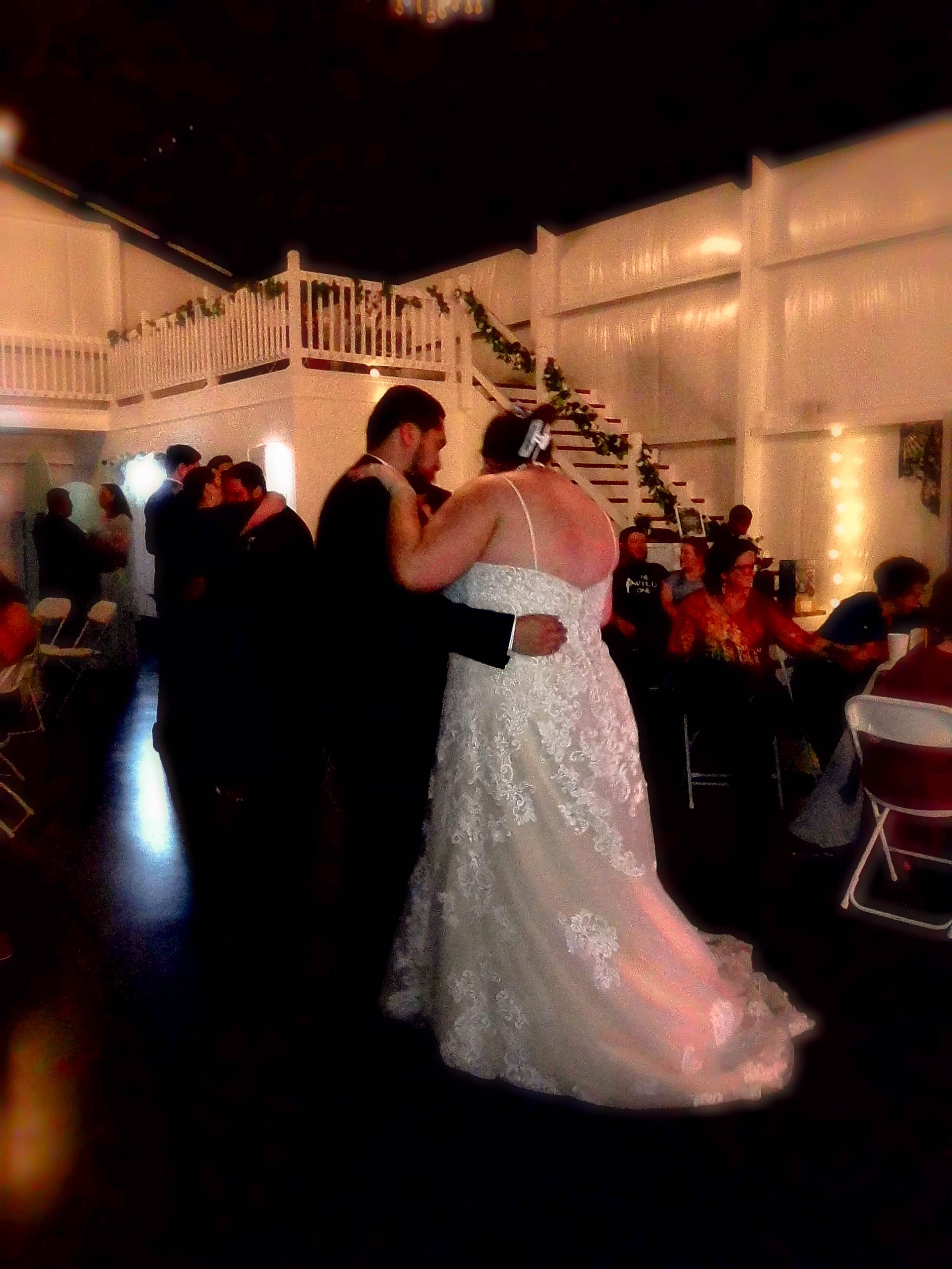 A bride and groom dancing together at their wedding reception, with guests seated at tables in the background.