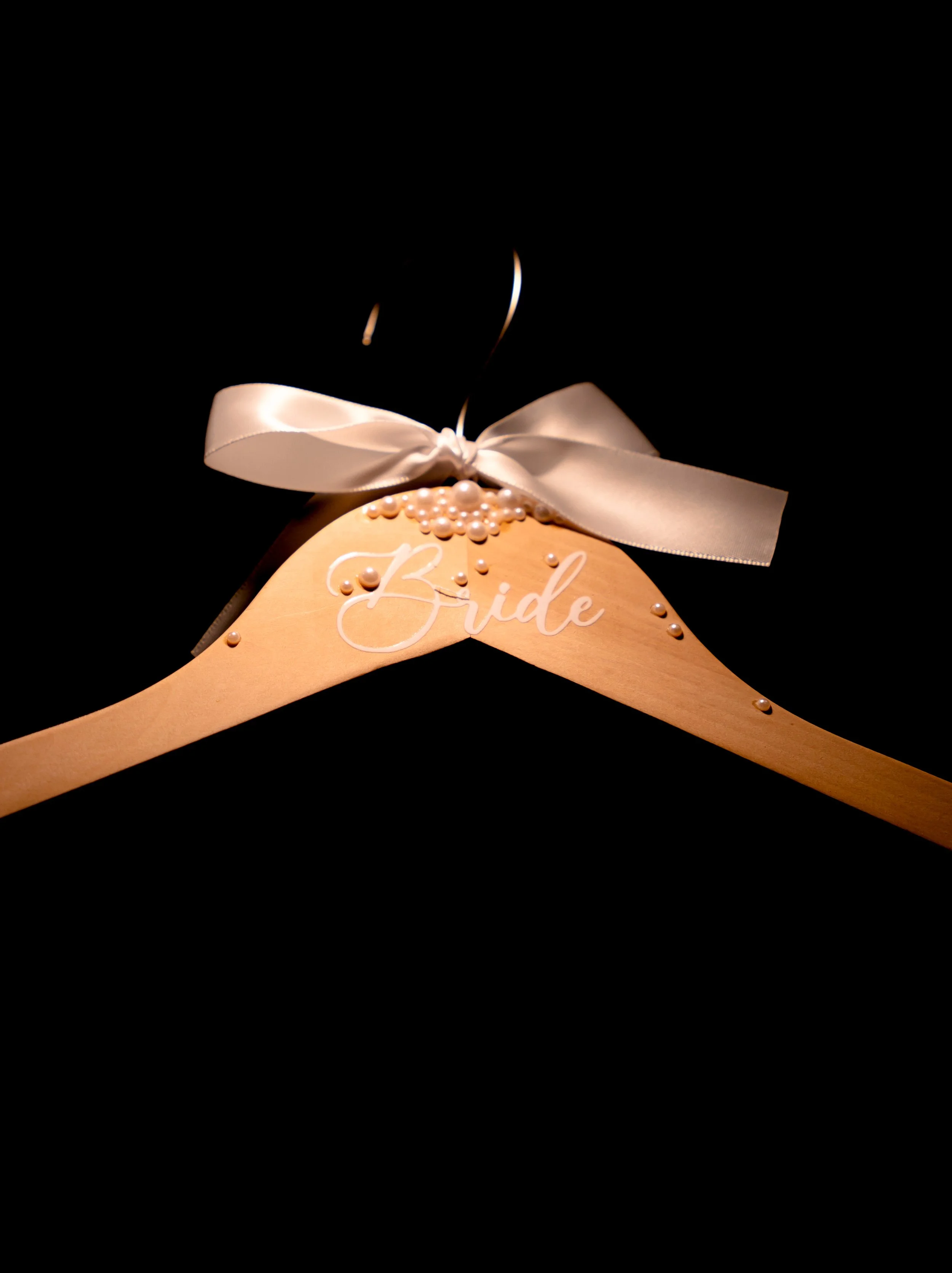 Wooden hanger decorated with pearls, a white ribbon tied in a bow, and the word "Bride" written in white, used for bridal dress hanging.