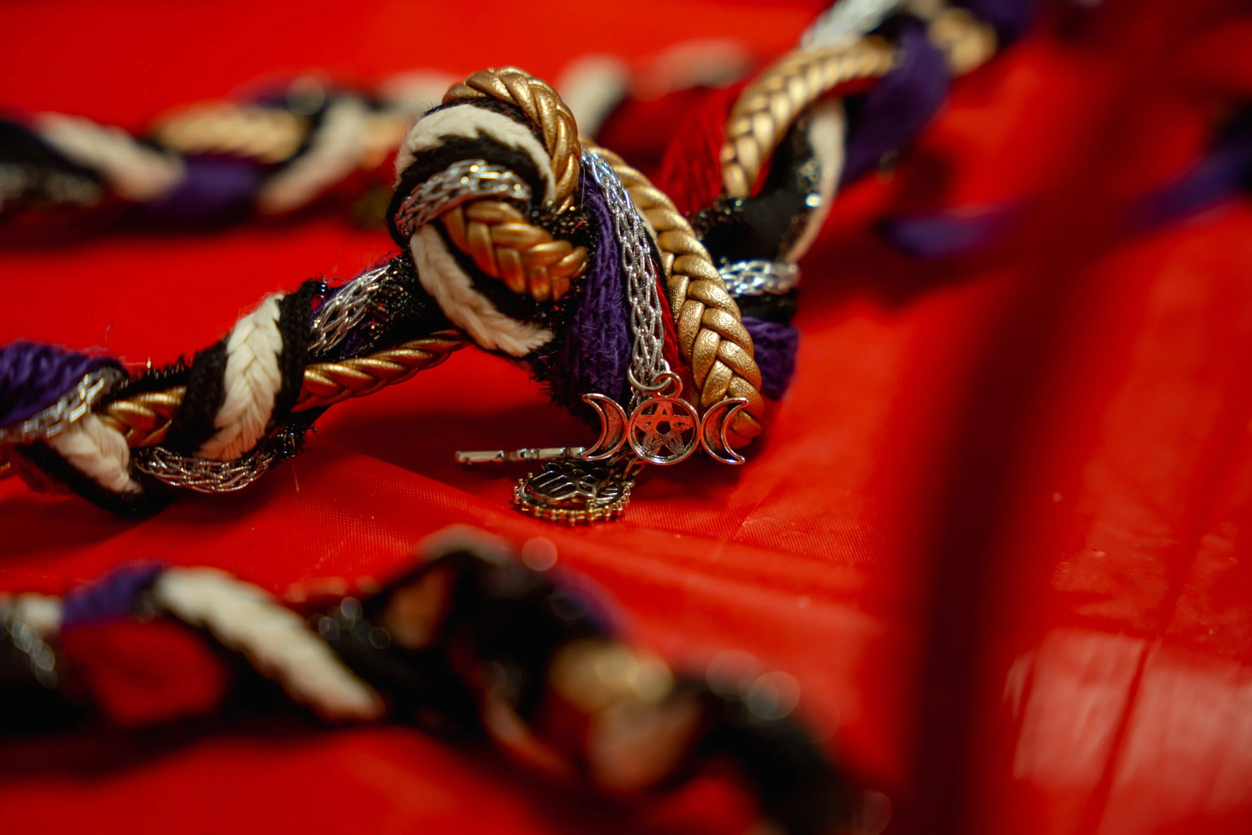 Close-up of a colorful braided cord with charms on a red fabric background.