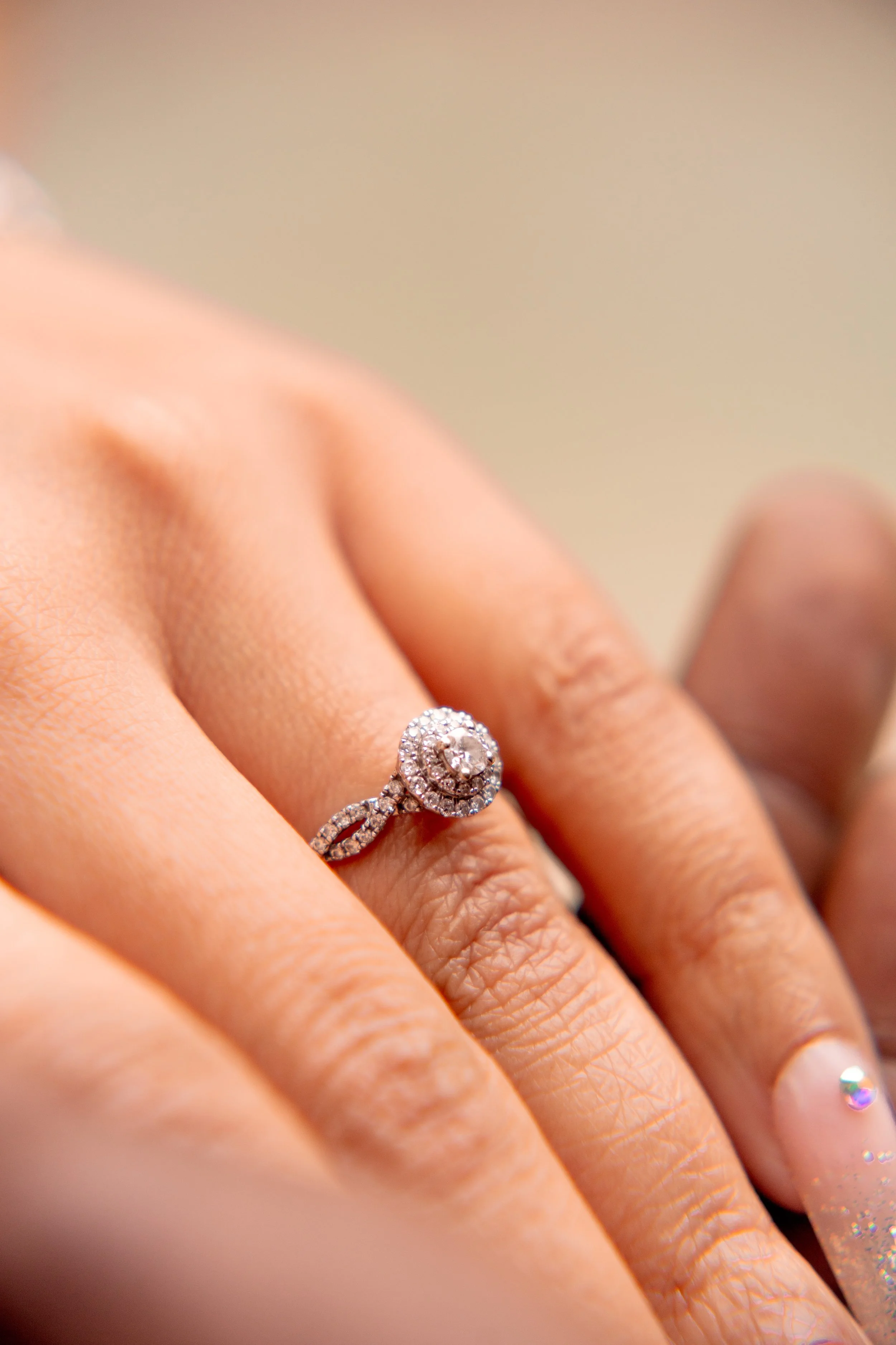 Close-up of a hand wearing a diamond engagement ring with a large central stone surrounded by smaller diamonds.