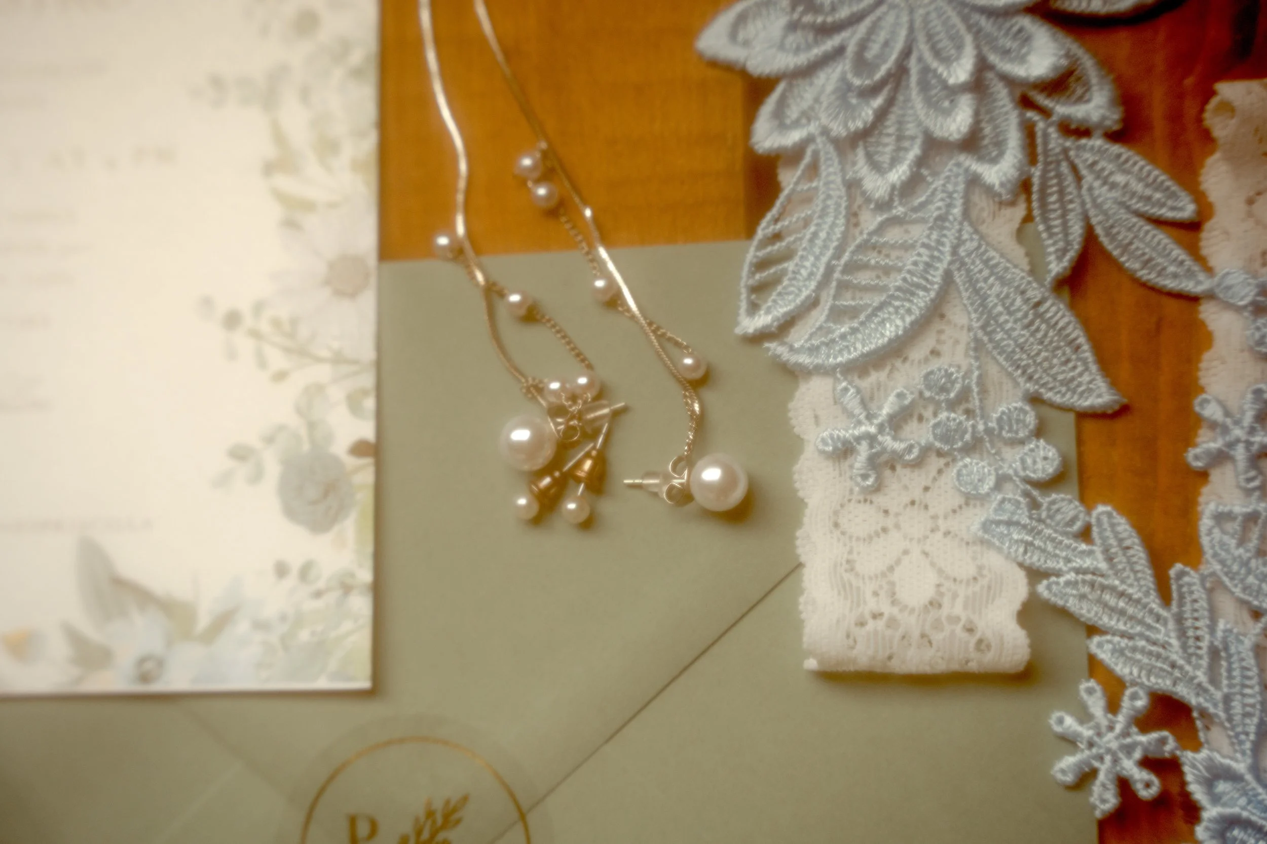 Set of pearl jewelry including necklace, earrings, and bracelet with lace and floral fabric on a wooden surface.