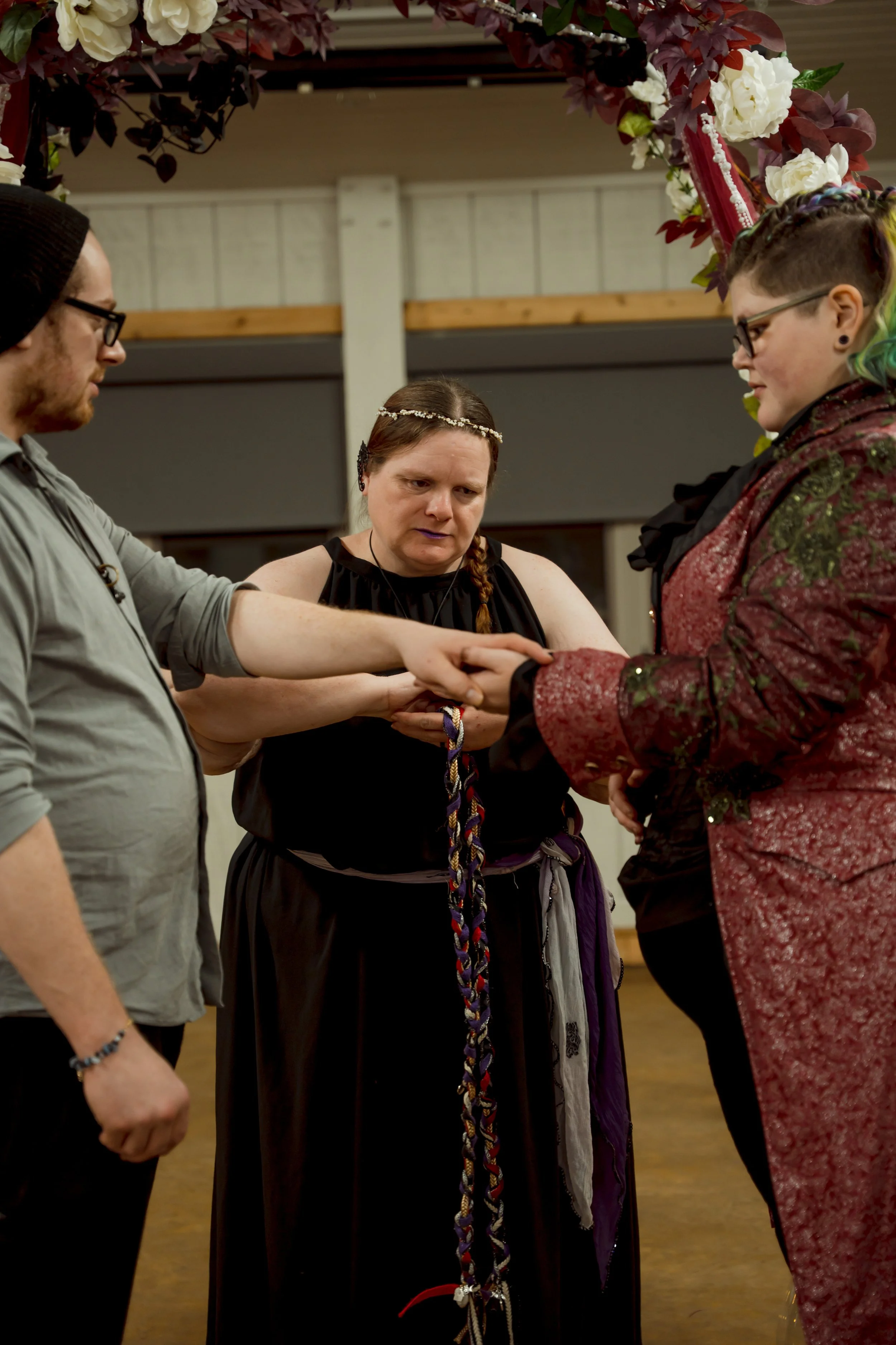 A group of four people participating in a ceremony or ritual, with one woman holding a braided cord while the others hold hands over her.
