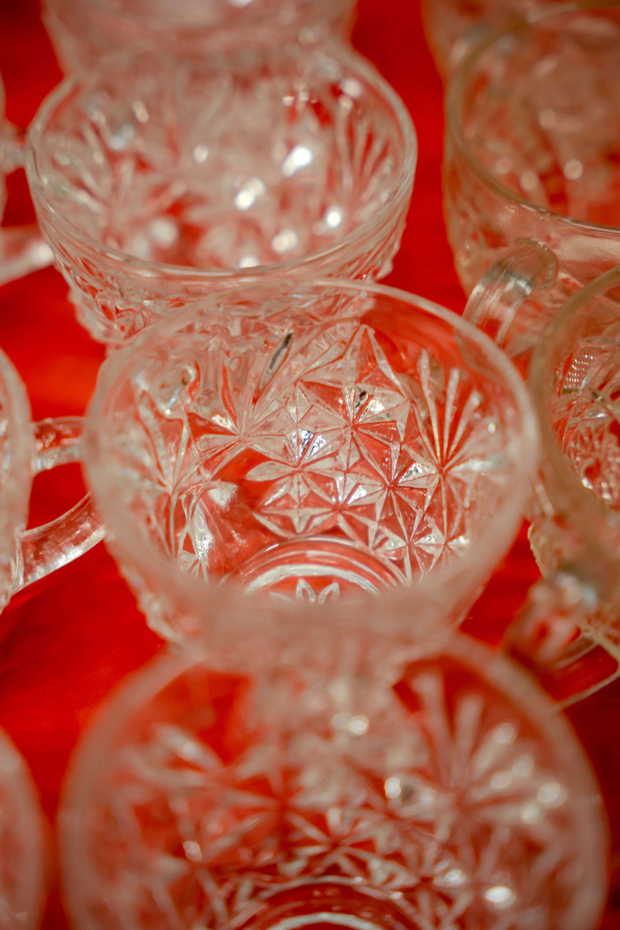 Close-up view of several clear glass cups with intricate patterns, placed on a red surface.