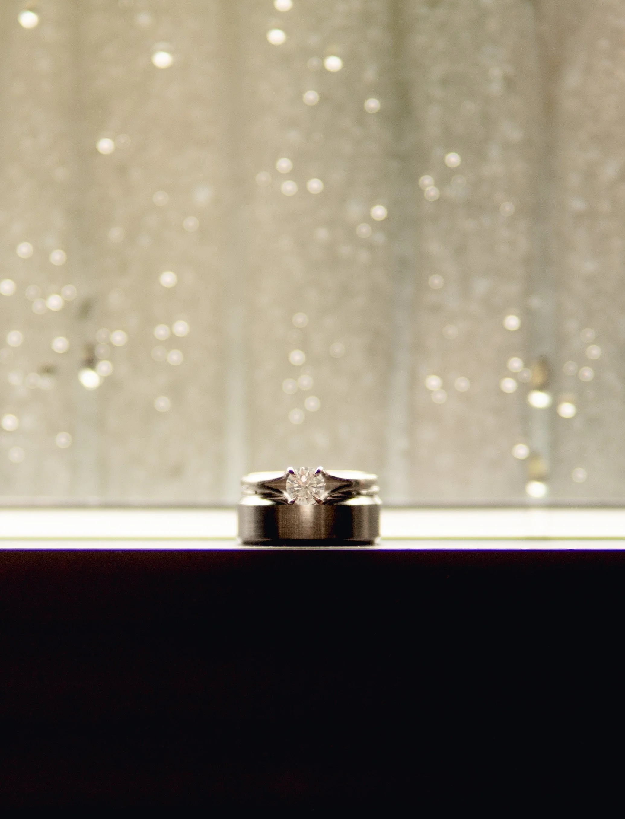 A diamond engagement ring on a dark surface with a blurred, sparkling background.