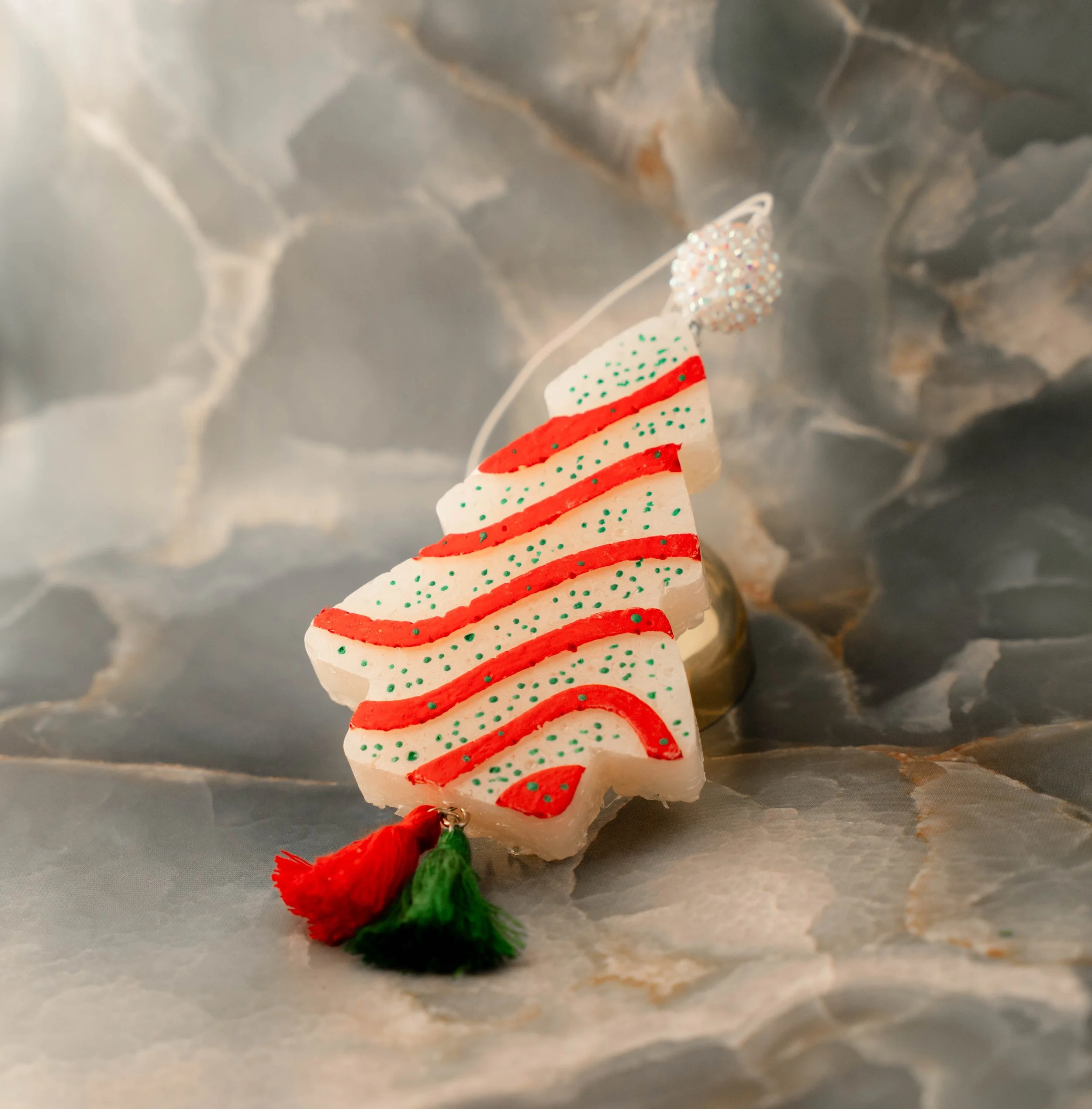 Christmas tree ornament shaped like a white Christmas tree with red and green accents, placed on a marble surface with a silver and gold background.