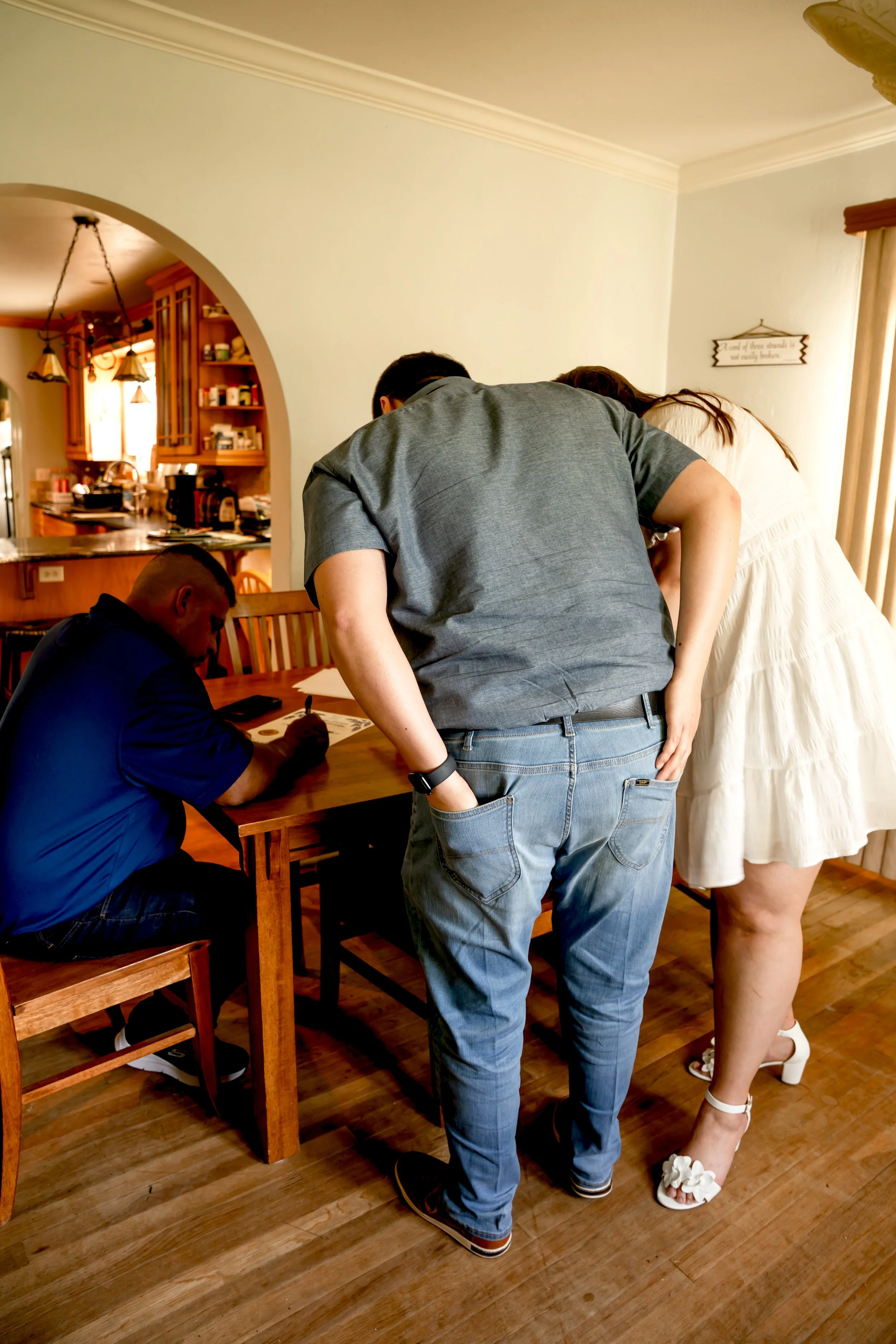 A man and woman examining something on a table while a third man seated writes or signs on a paper.