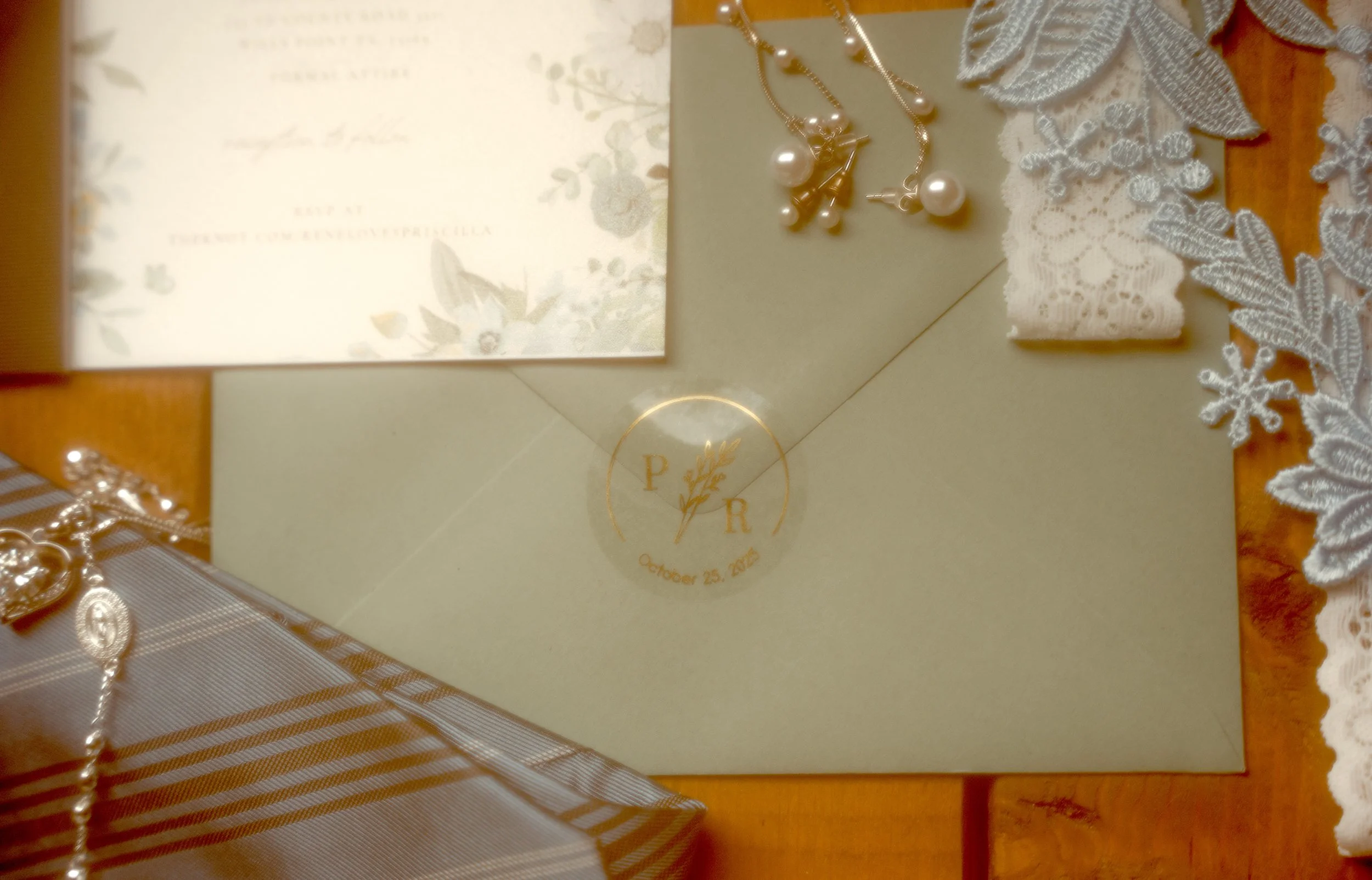 Wedding invitation, pearl necklace, lace fabric, and a silver gift box on a wooden surface.