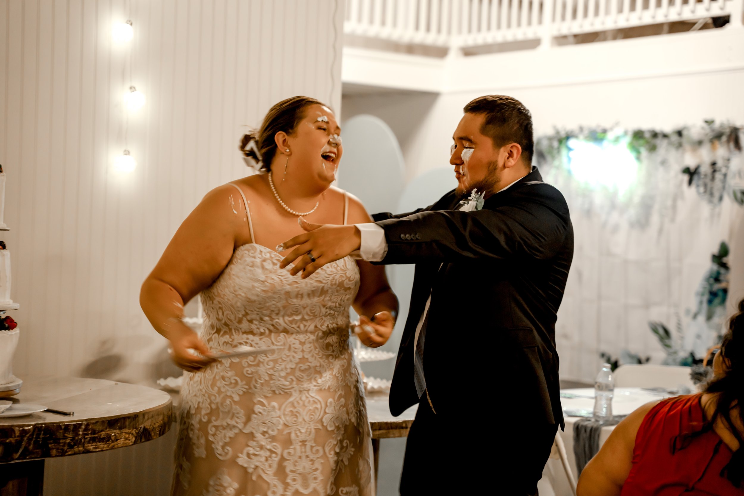 A couple celebrating at their wedding, covered in cake and frosting, smiling and laughing.