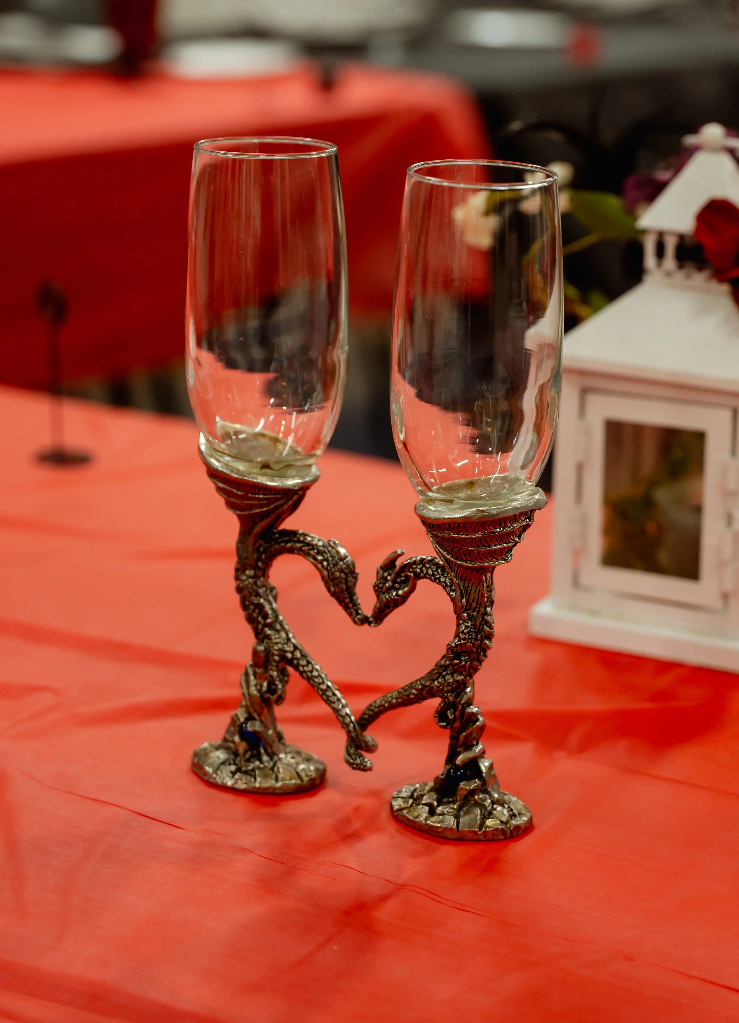 Decorative glass holder with two champagne flutes on heart-shaped dragon leg bases, placed on a pink tablecloth.