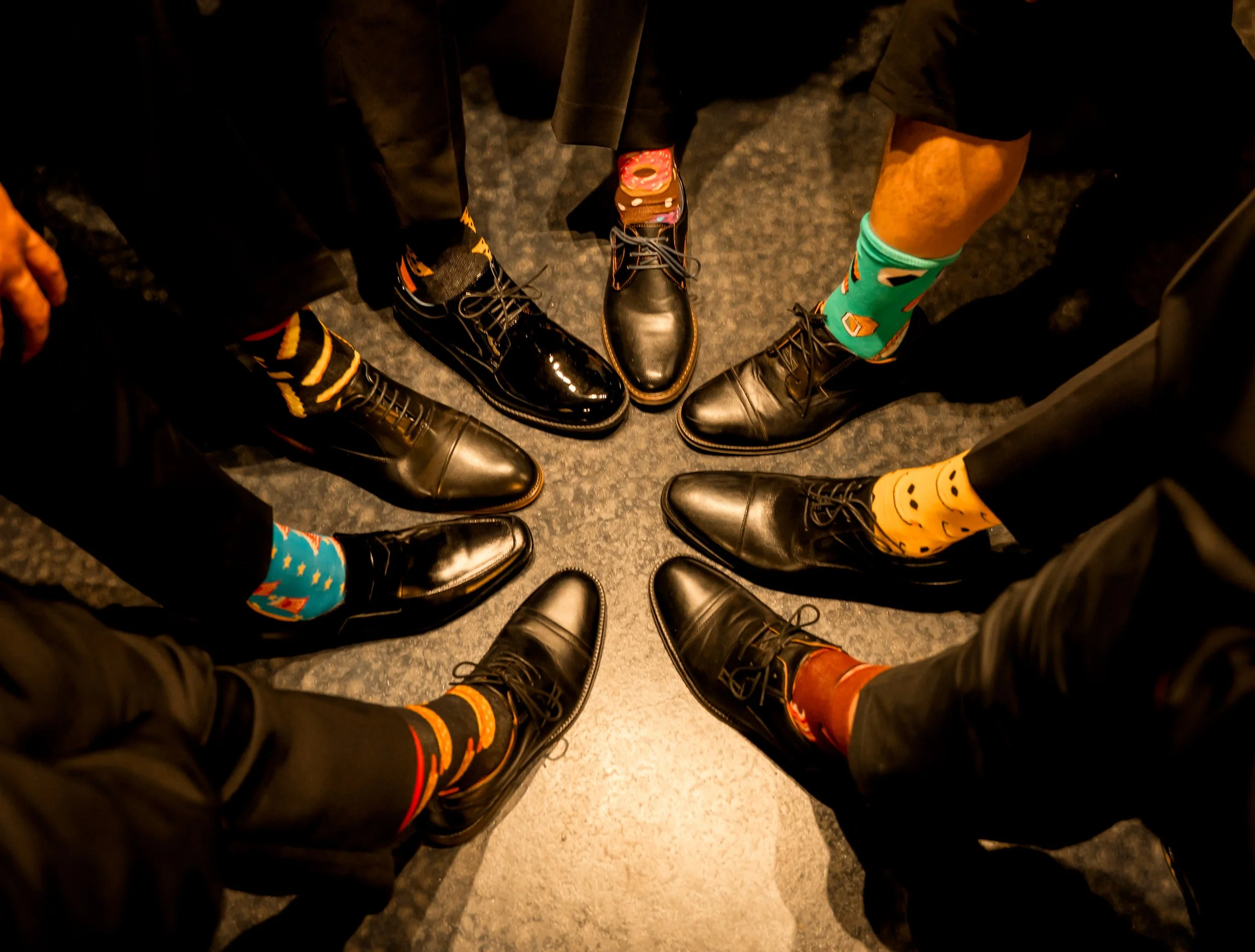 Group of people standing in a circle showing their shoes and colorful socks.