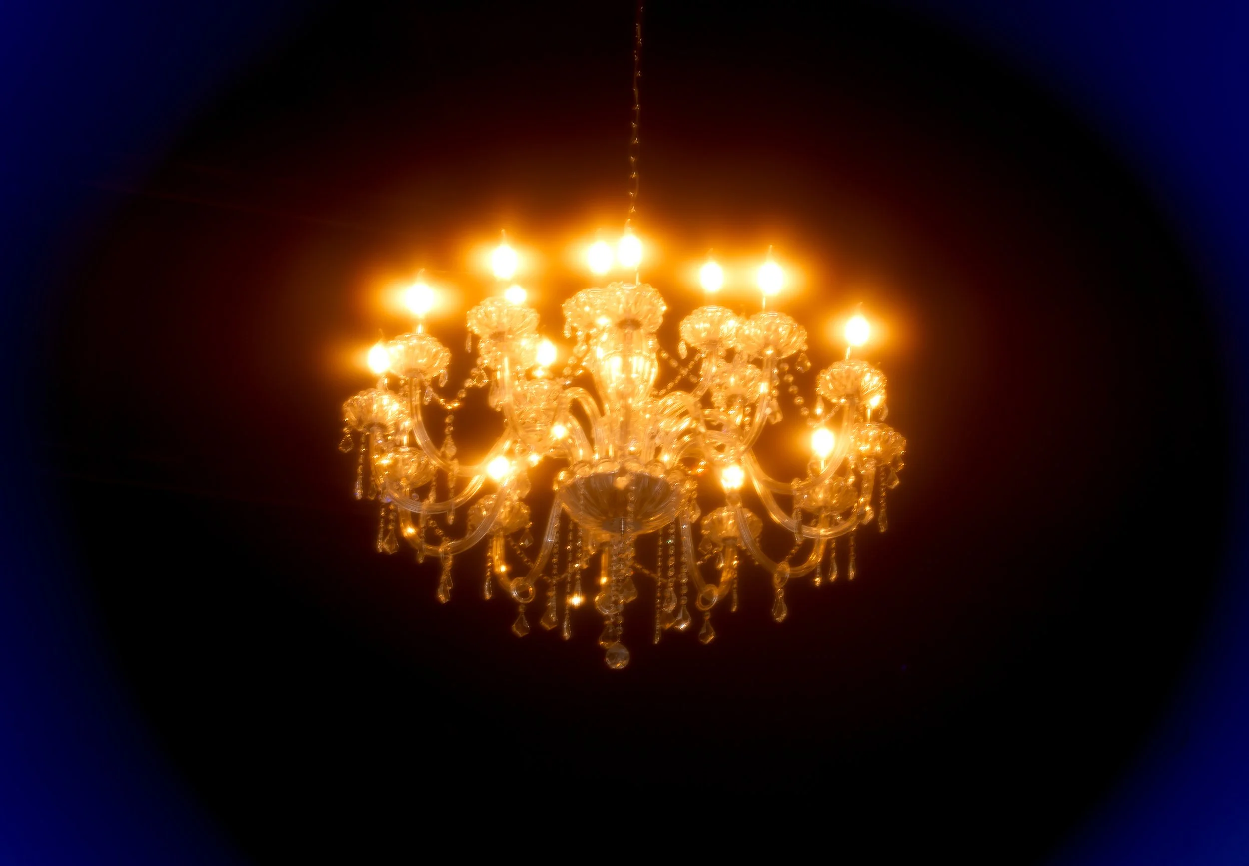 A gold ornate chandelier with multiple lit candles hanging from the ceiling.