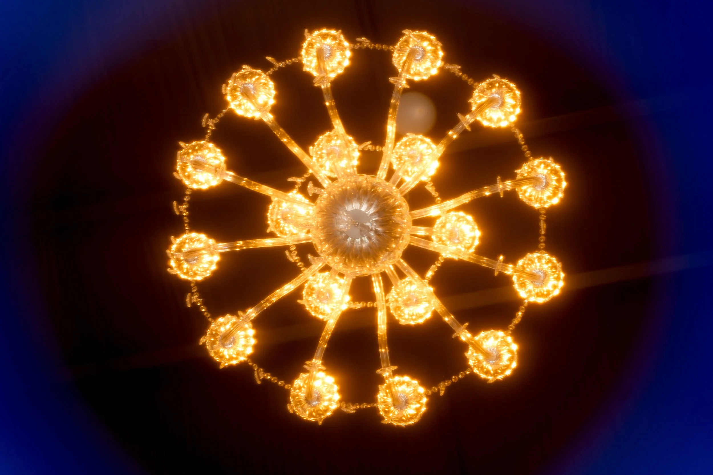 A decorative chandelier with multiple glowing lights hanging in a dark space.