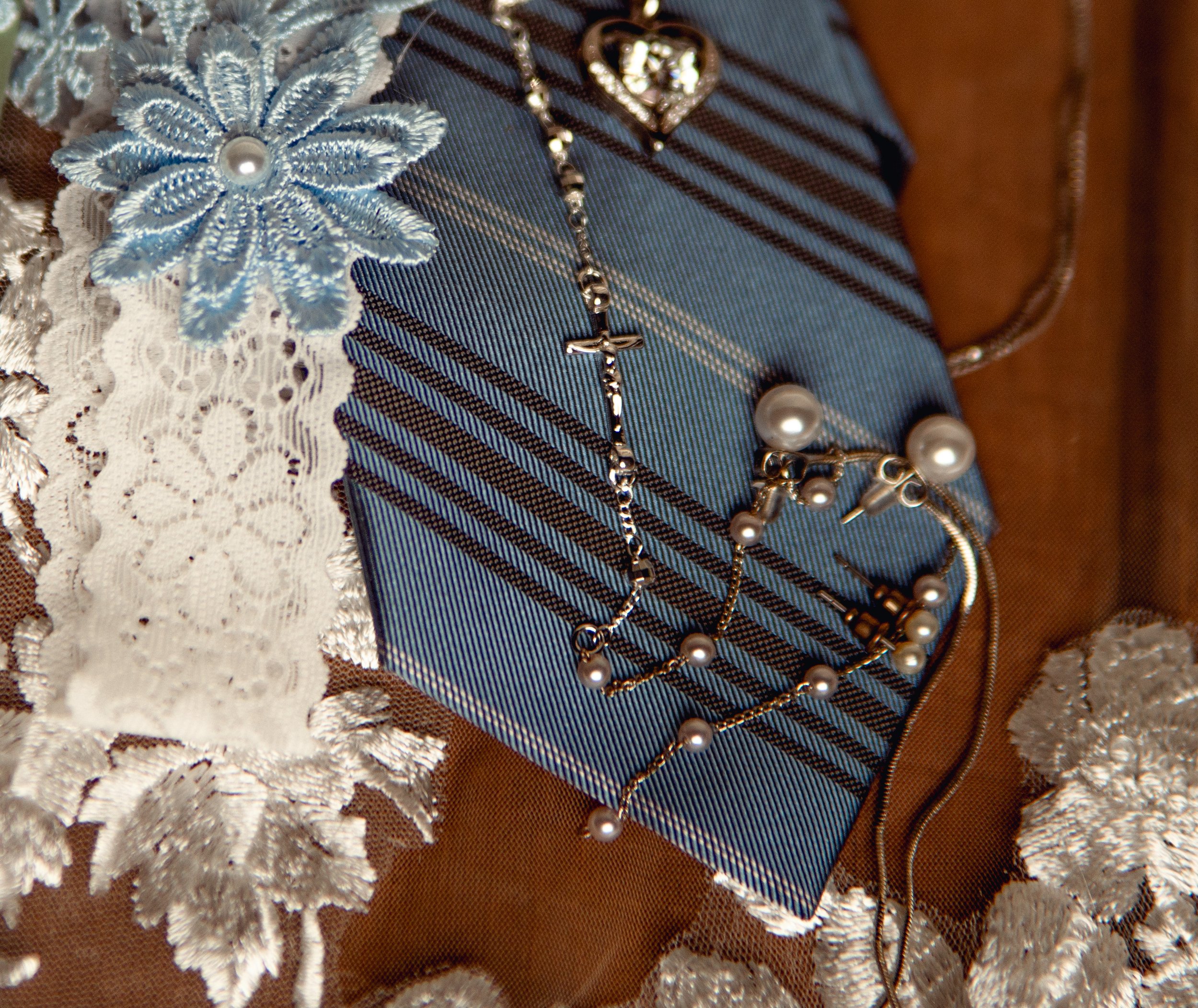 A collection of pearl jewelry including a necklace and earrings, placed on a blue striped cloth, with a lace and embroidered decorative cloth underneath.