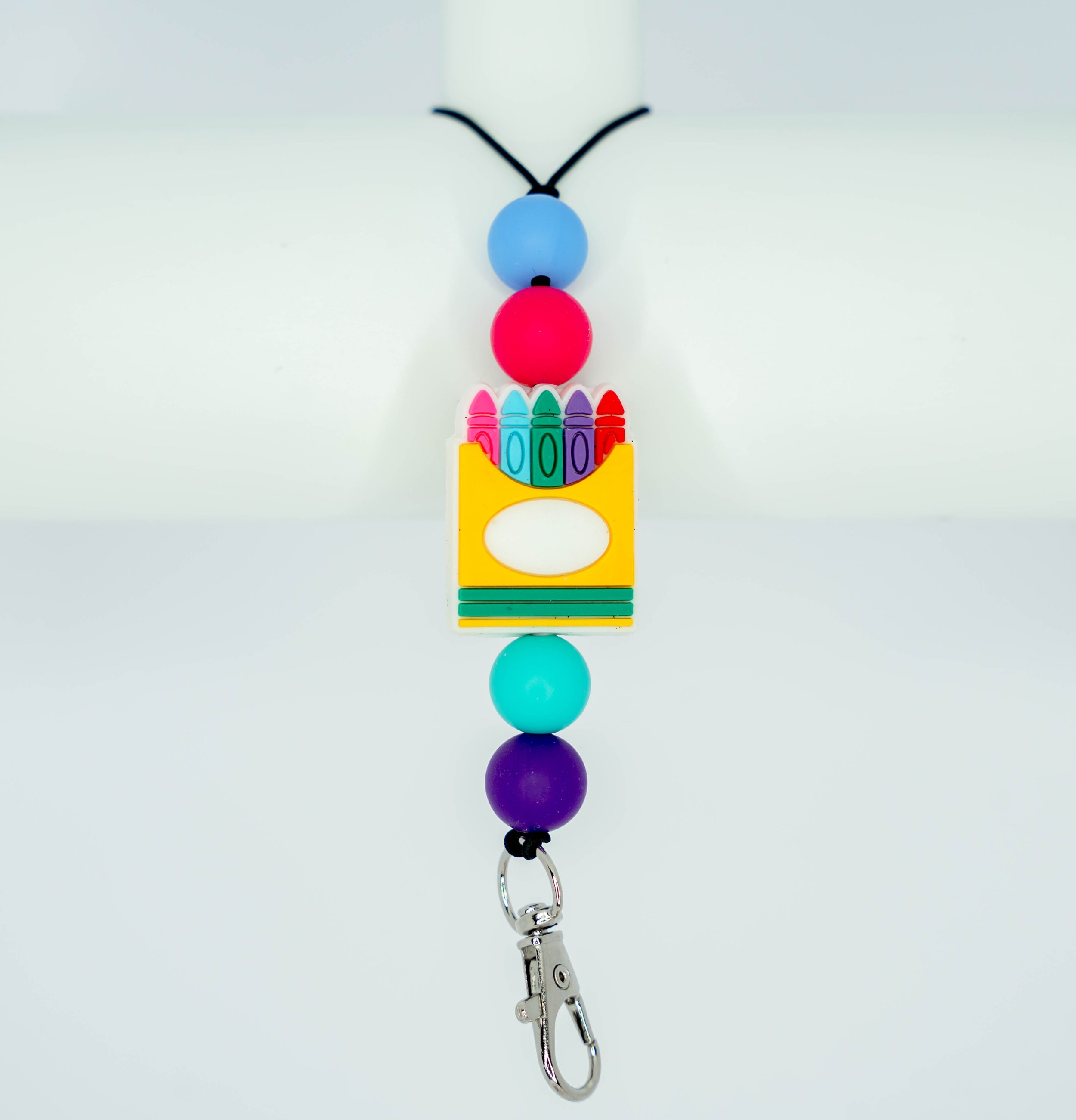 Colorful beaded keychain with a small yellow puzzle piece, a pink, red, green, purple, and blue bead, and a pair of small black antennae at the top.