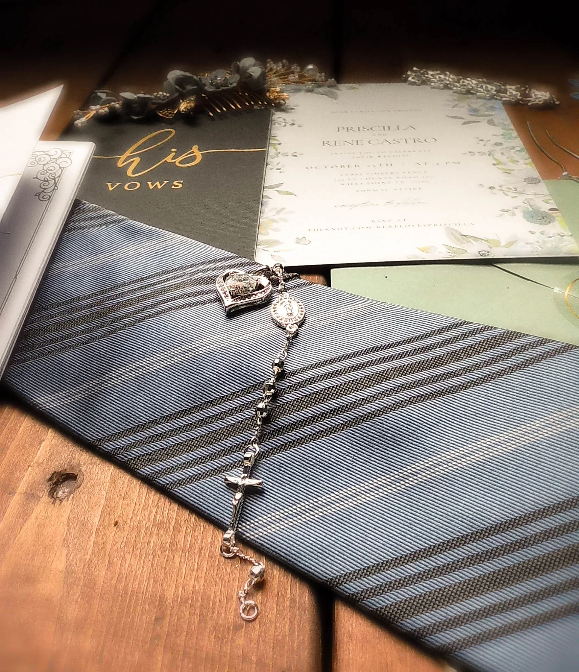 A collection of wedding or event invitations and jewelry, including a rosary, on a wooden surface.