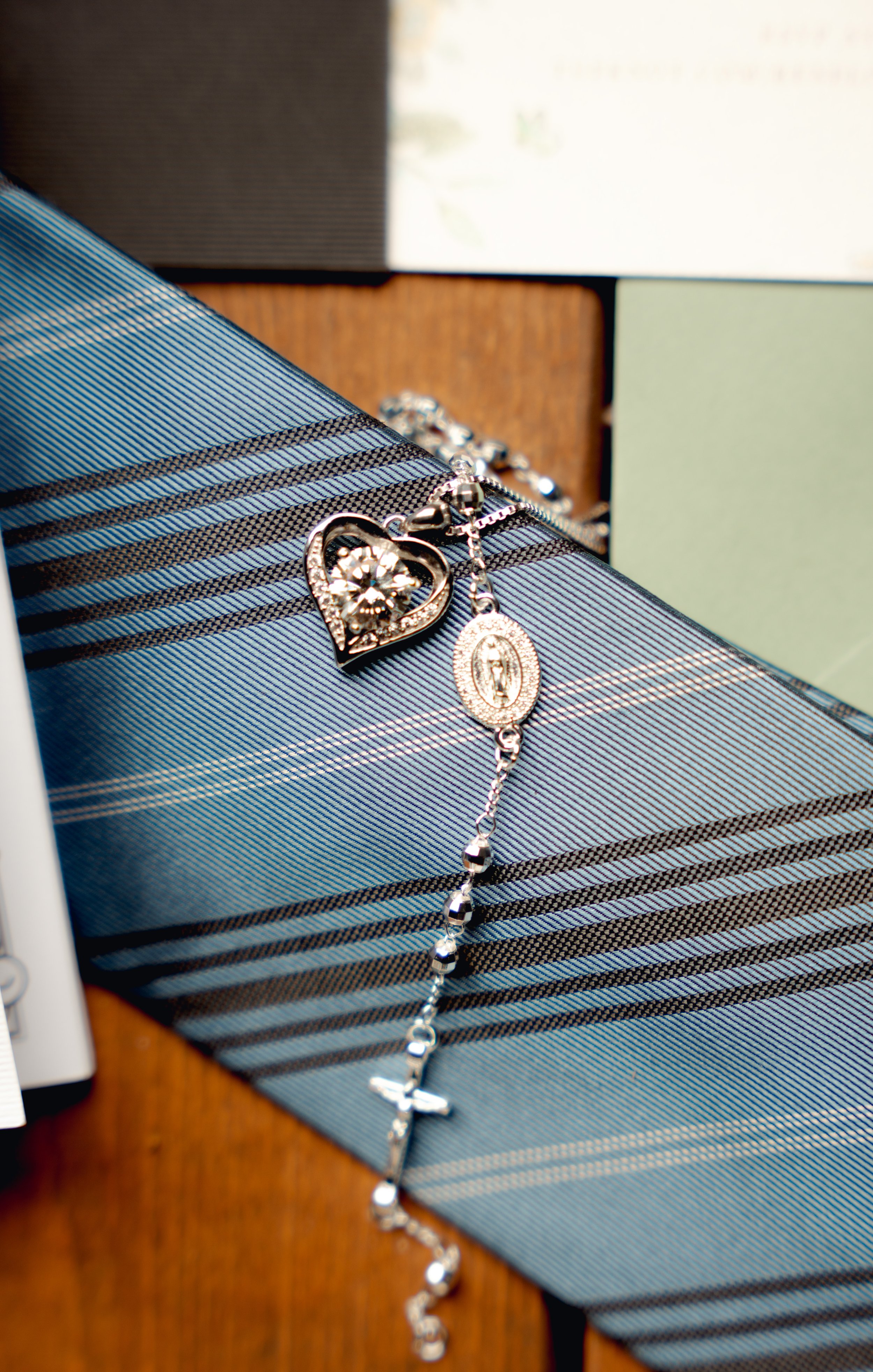 Silver jewelry with heart and religious medallion charms resting on blue striped fabric.
