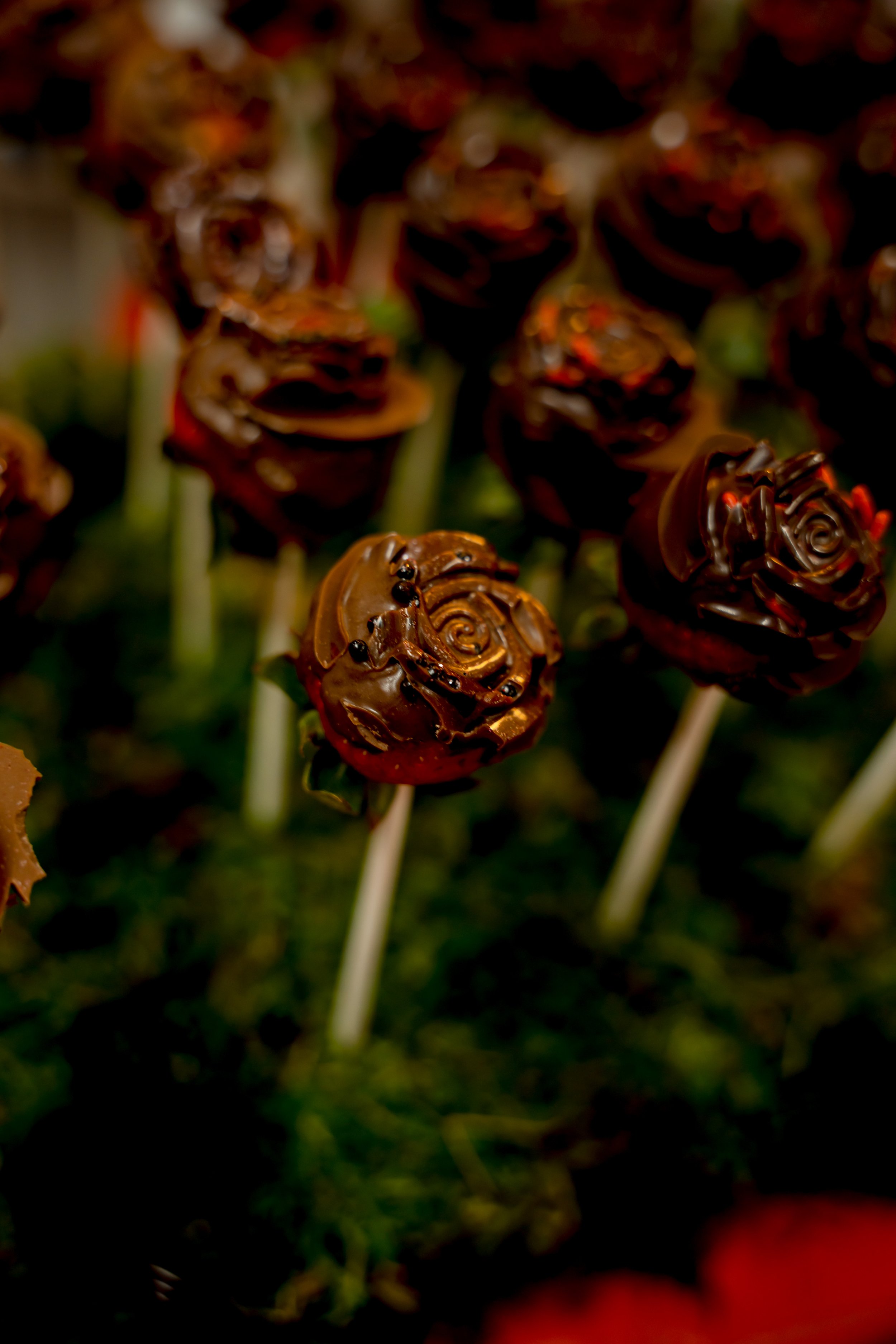 Chocolate lollipops shaped like roses on sticks, displayed outdoors.
