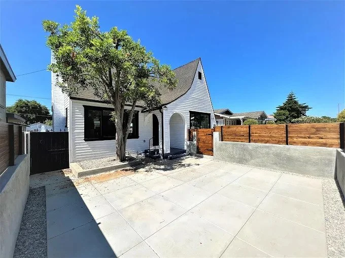 Fully renovated white cottage-style home exterior with black-framed windows, new paver patio and wood fence in Los Angeles, California