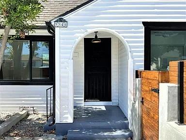 Renovated arched entry porch with black door and wood gate on a white lap-siding home in Los Angeles, California