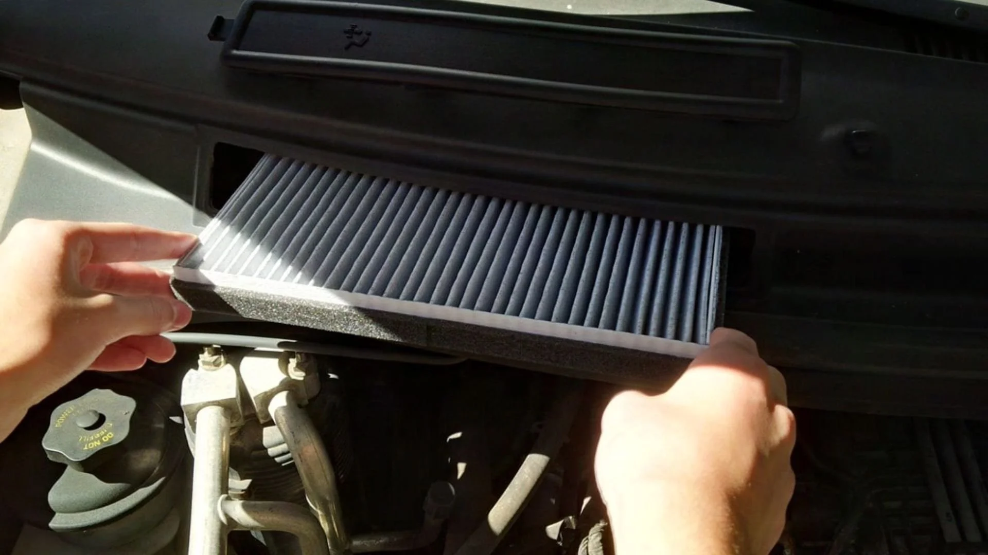 A person installing a new air filter into a vehicle's air filter compartment in the engine bay.