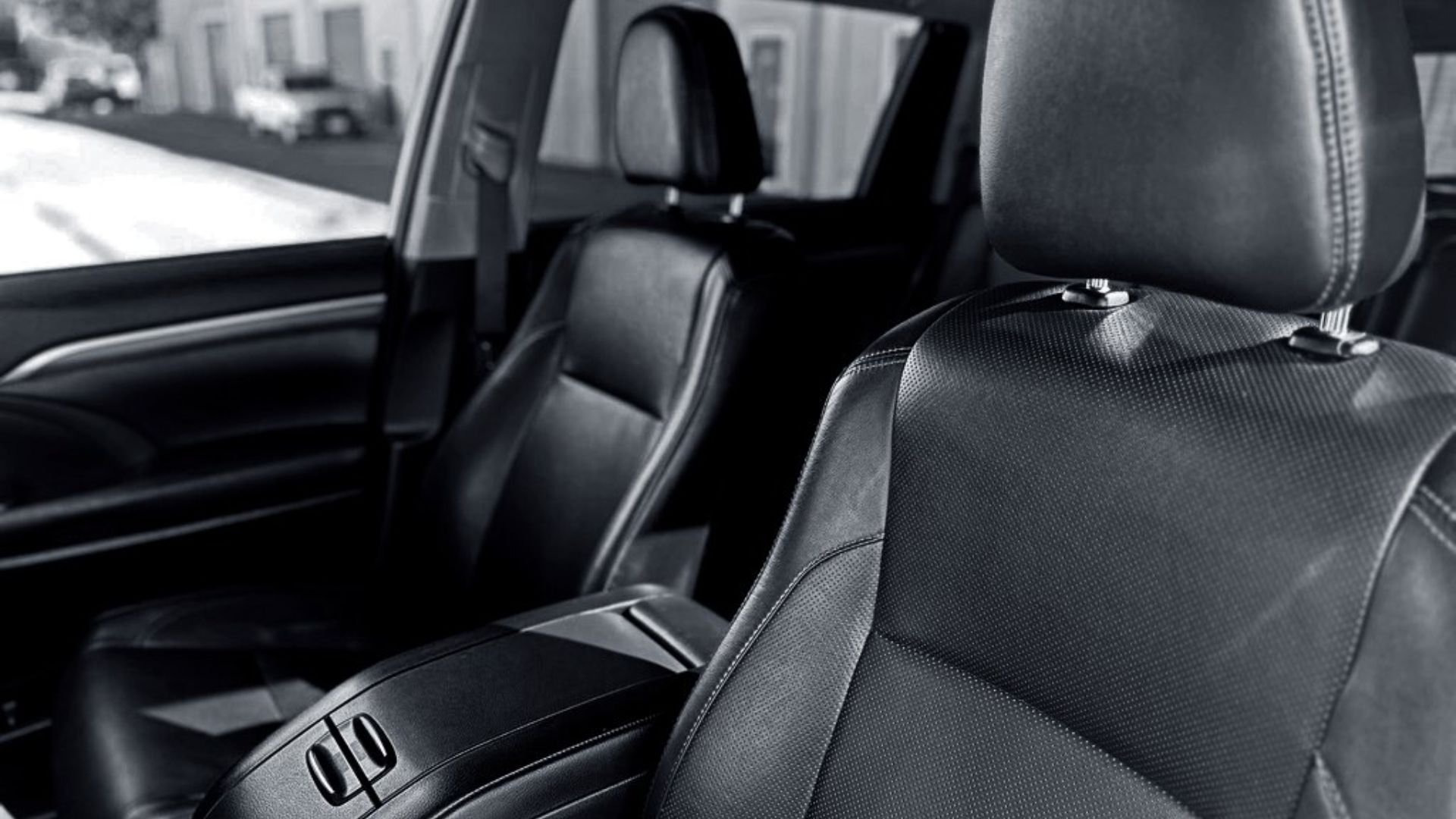 The interior of a vehicle showing black leather seats with detailing and headrests, with a blurred view of the outside street through the windows.