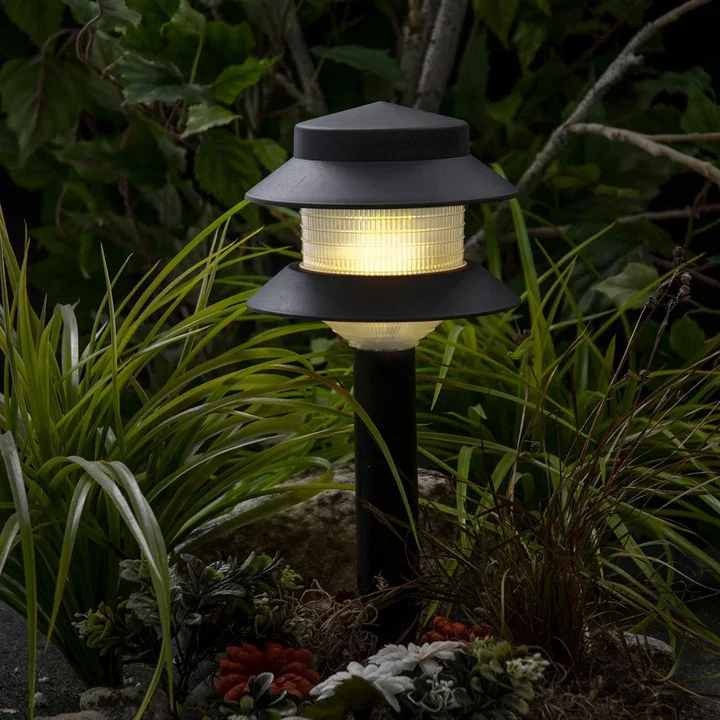 Outdoor garden lamp illuminating surrounding green and red plants at night