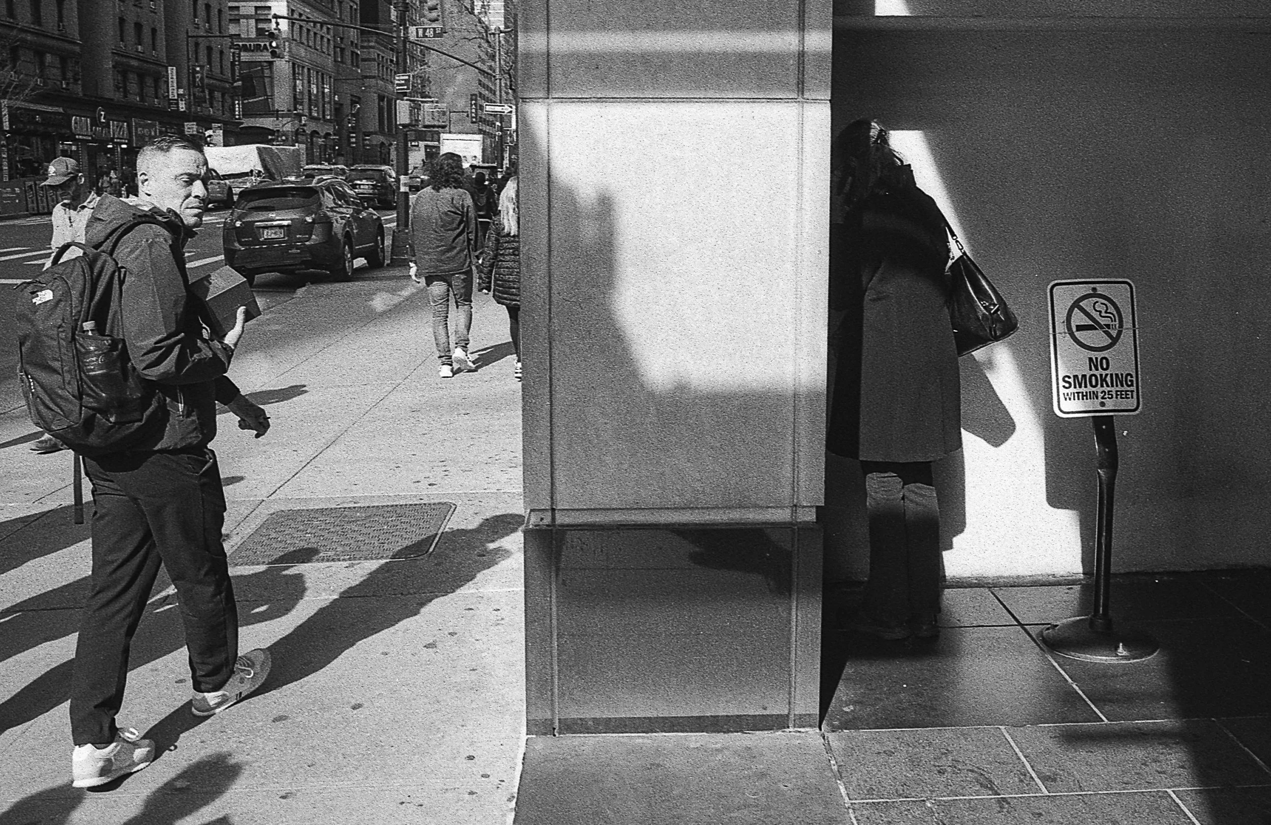 Black and white street scene with a person walking and a 'No Smoking' sign.