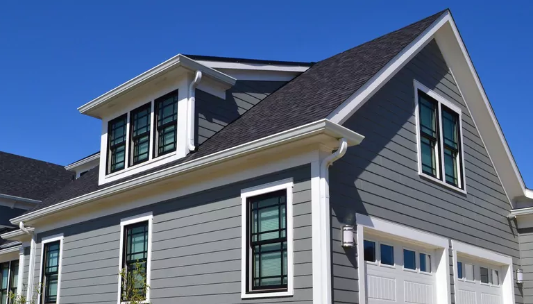 Modern gray house exterior with black-framed windows and a dark shingled roof under a clear blue sky.
