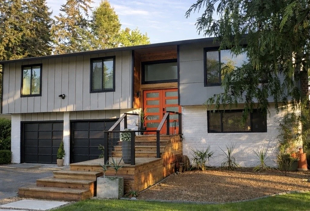 Modern two-story house with a combination of white brick and gray siding, black-framed windows, and a wooden front door, accessed by a wooden staircase.