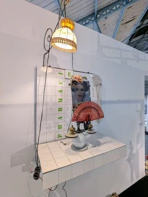 Decorative display with a framed portrait of a woman, a red folding fan, a small decorative table, a patterned lamp, and a tiled countertop against a white wall.